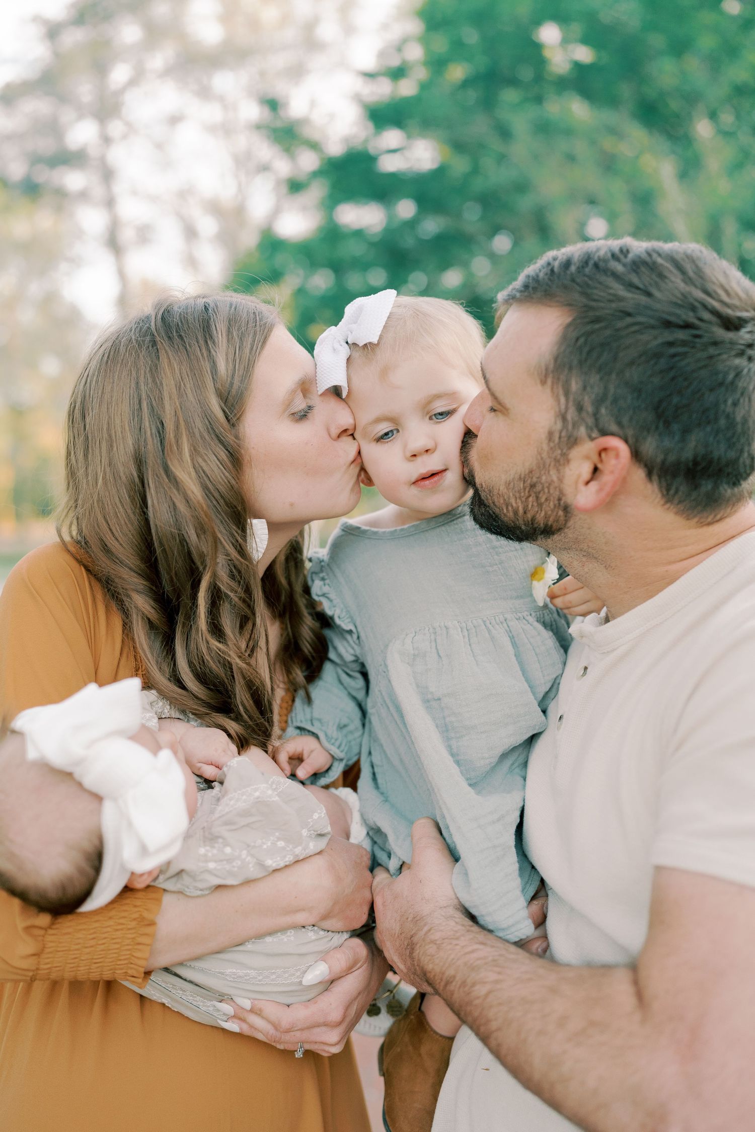 A loving family shares tender kisses with their baby in a series of outdoor portrait photos.