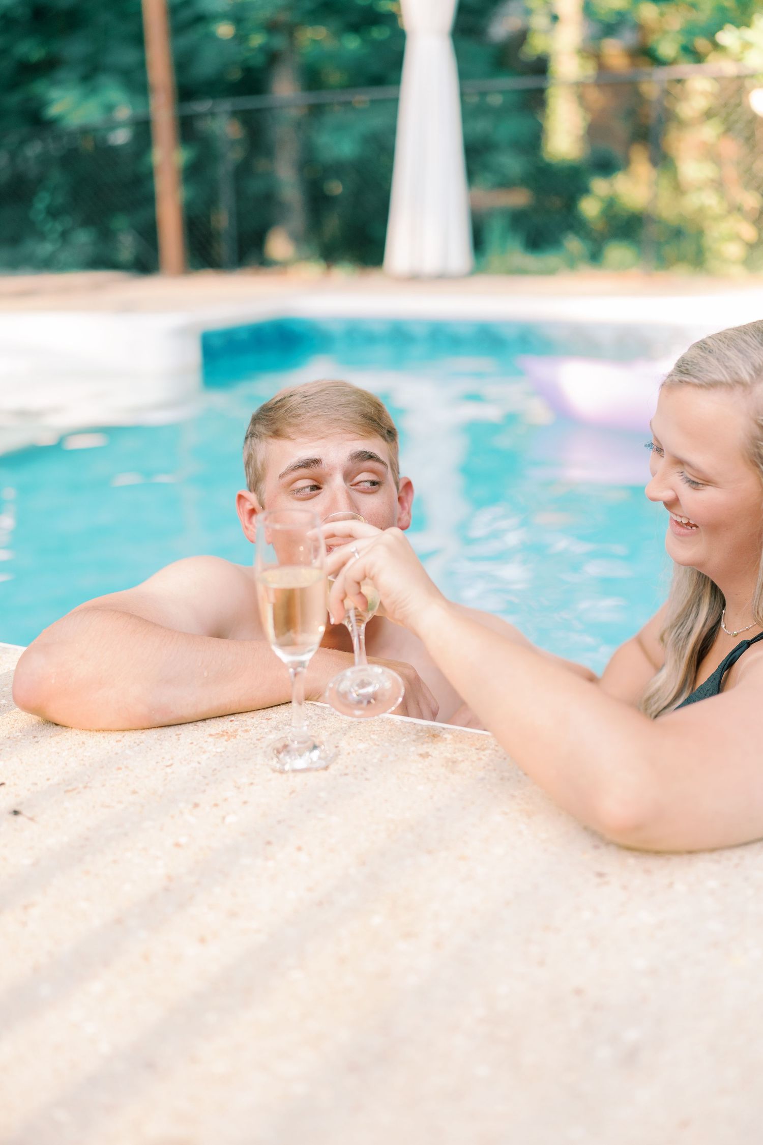 Couple relaxing on pool edge with drinks during outdoor summer photoshoot.