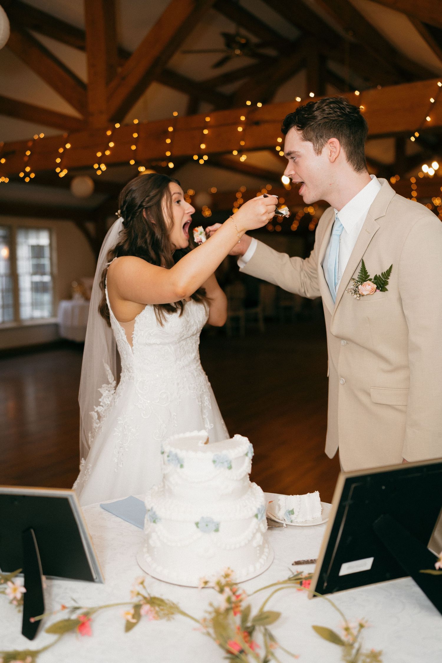 Newlyweds playfully feed each other wedding cake at their reception.