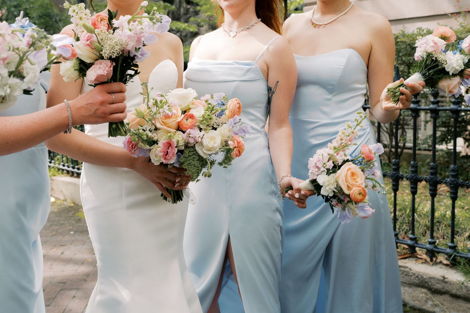 Wedding party members in light blue dresses holding peach and white floral bouquets.