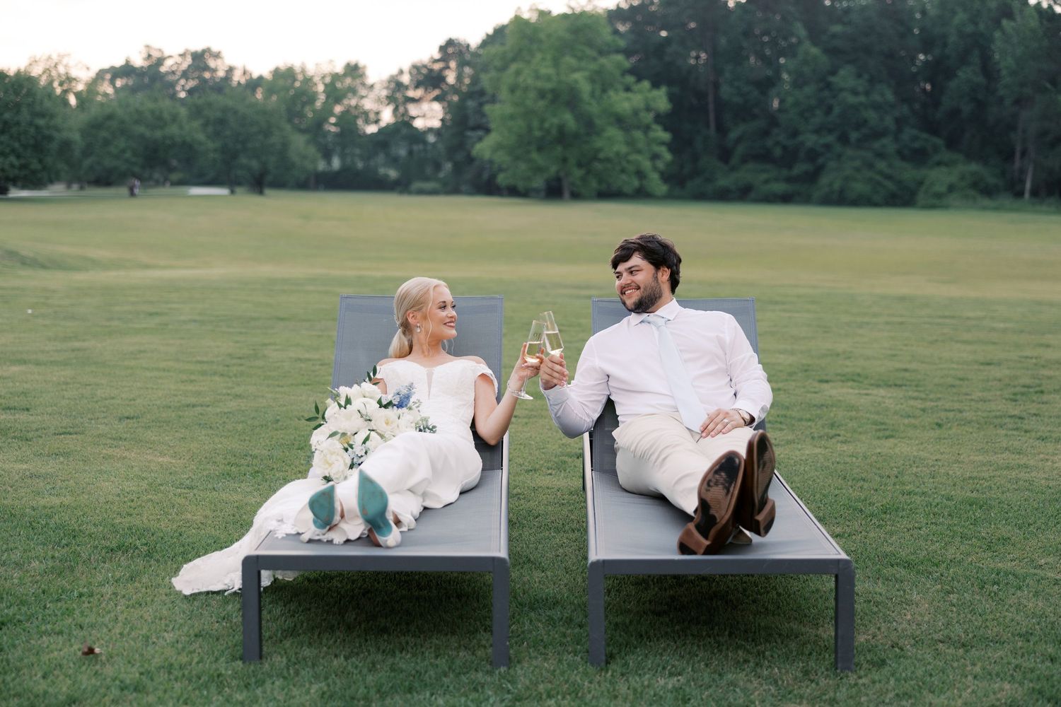 Wedding couple relaxing on outdoor lounge chairs in a grassy field at sunset.