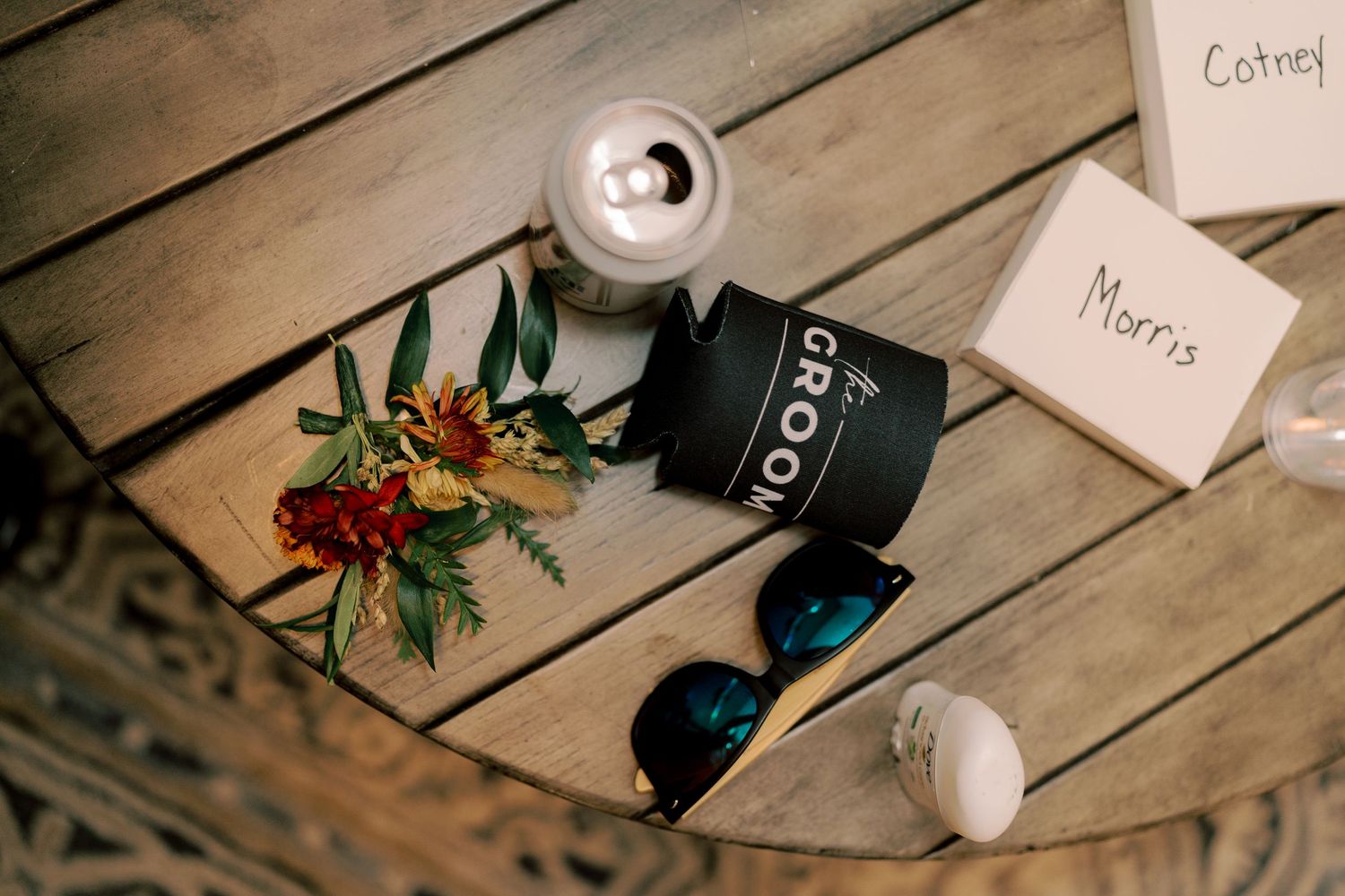 Wedding details including sunglasses and floral arrangement on wooden surface.