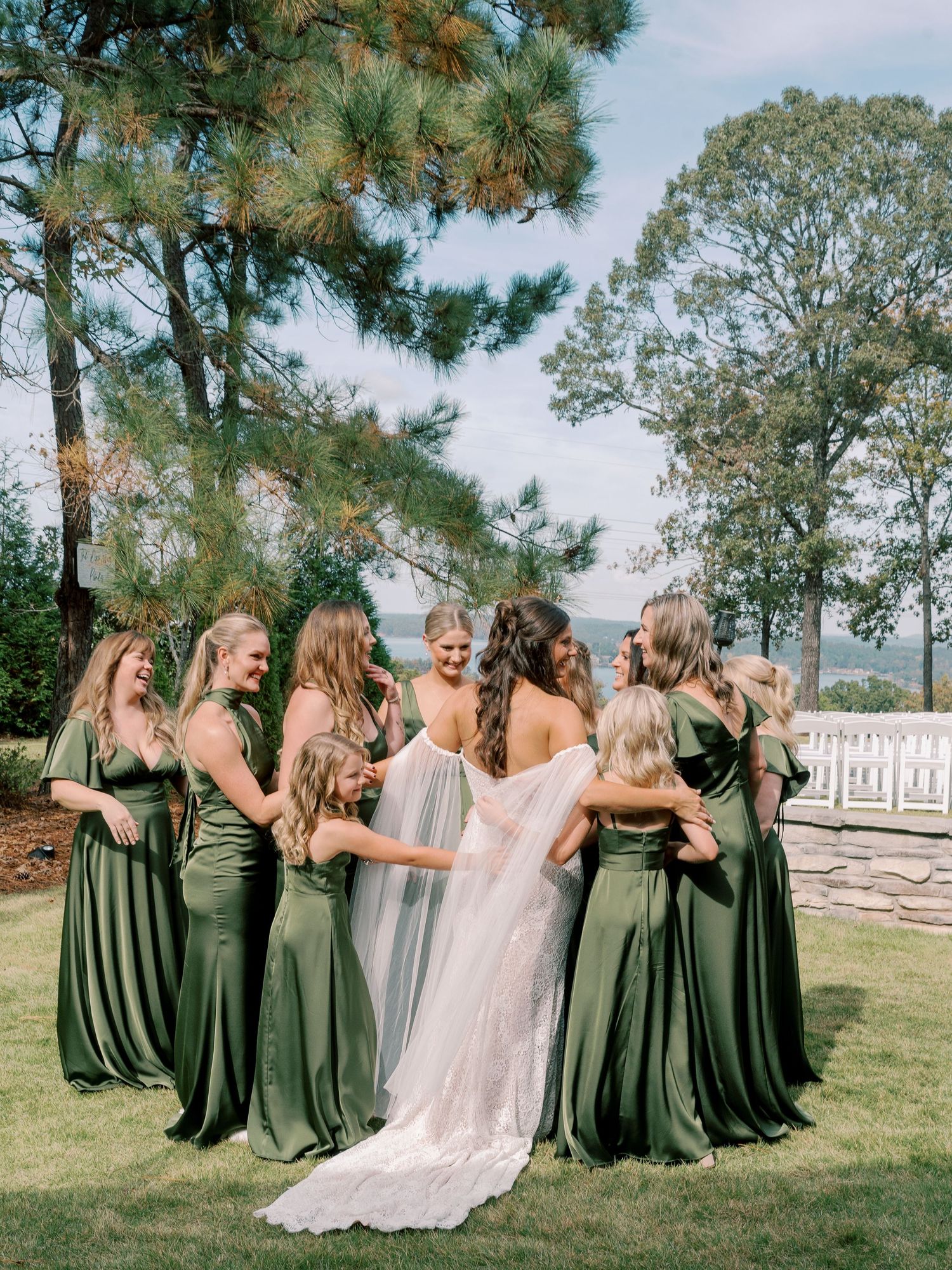 Wedding party in olive green dresses and white gown pose together outdoors on a sunny day.