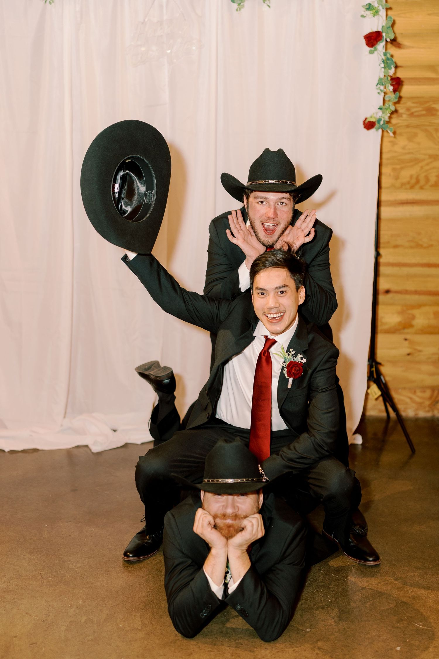 Playful wedding photos of groomsmen in black suits posing with cowboy hats.
