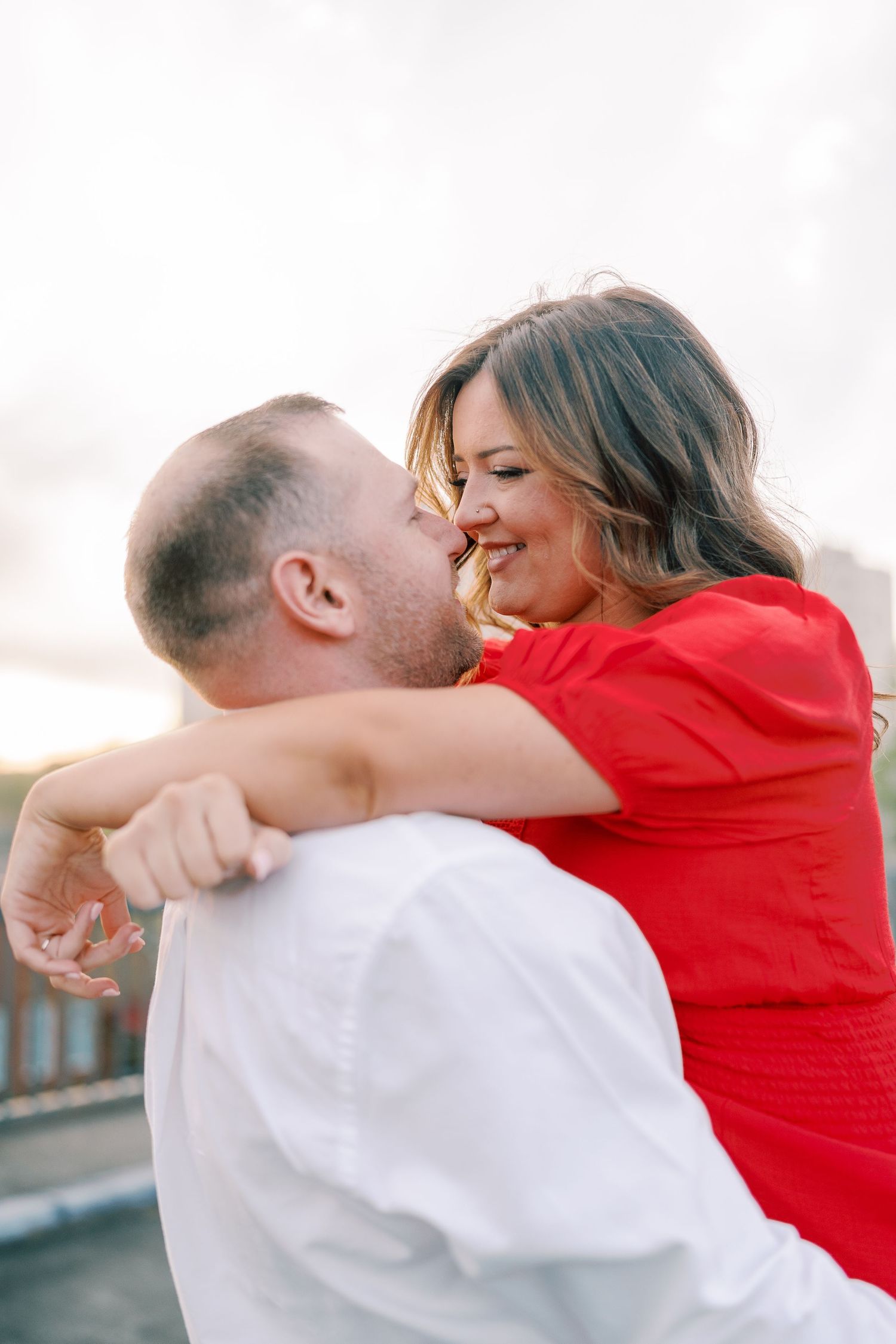 Couple in red and white share an intimate embrace against an urban backdrop.