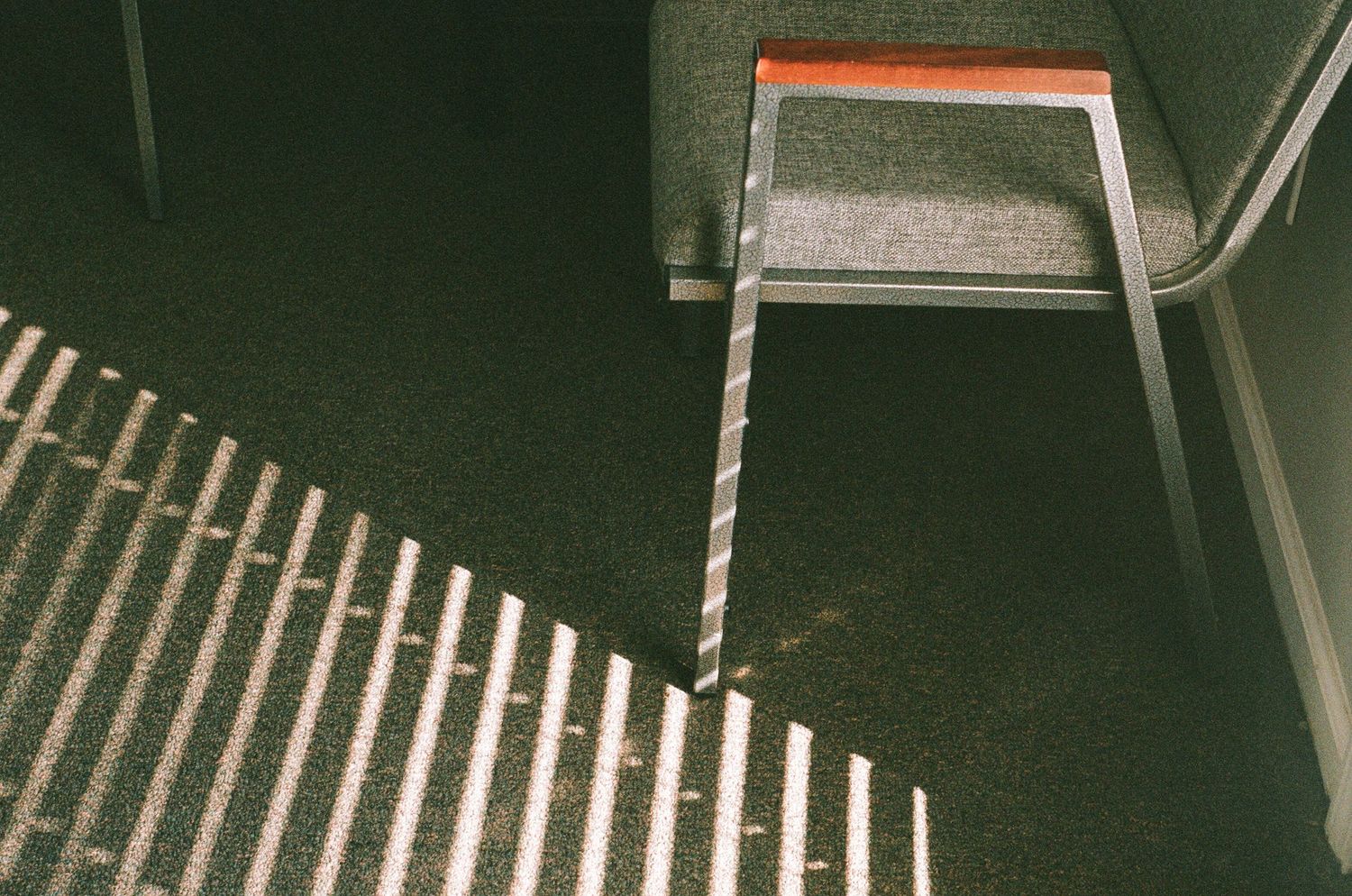 Light from window blinds creates dramatic shadows and lines on a dark carpeted floor.