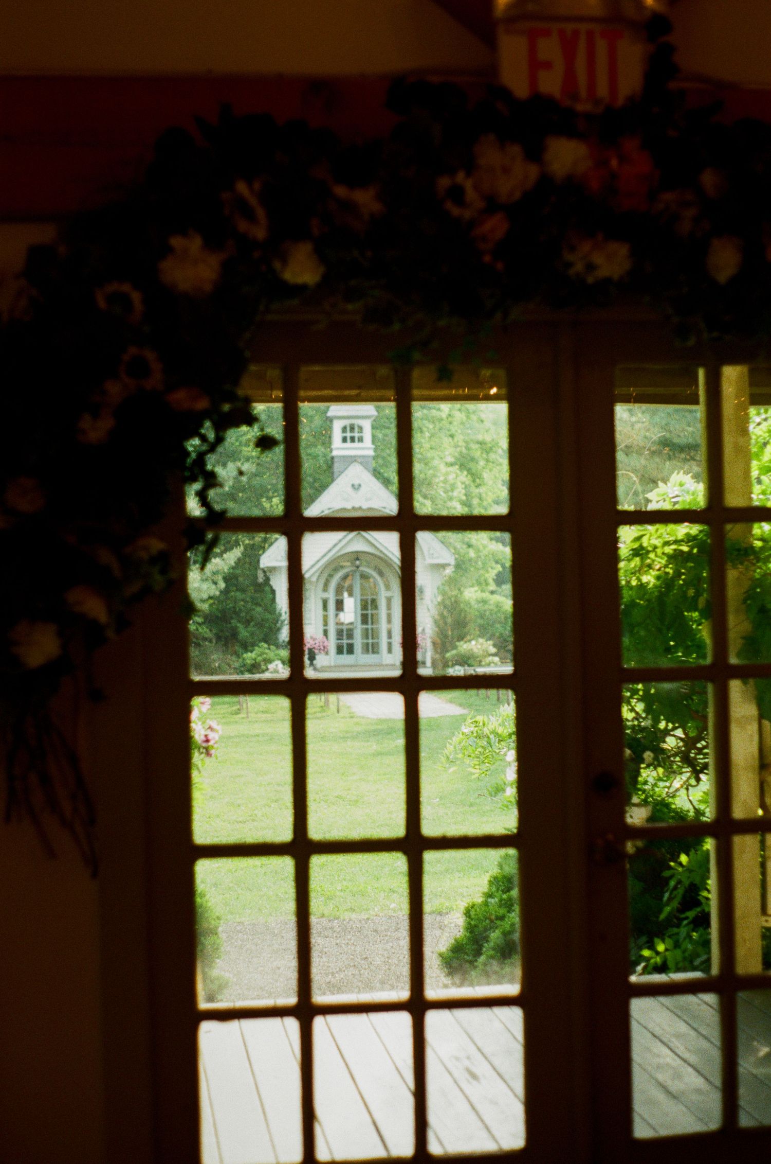 View through a window framed with floral garlands showing a small white chapel in the distance.