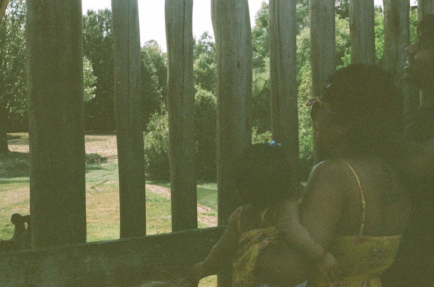 Silhouetted figure viewed through wooden fence posts in natural lighting.