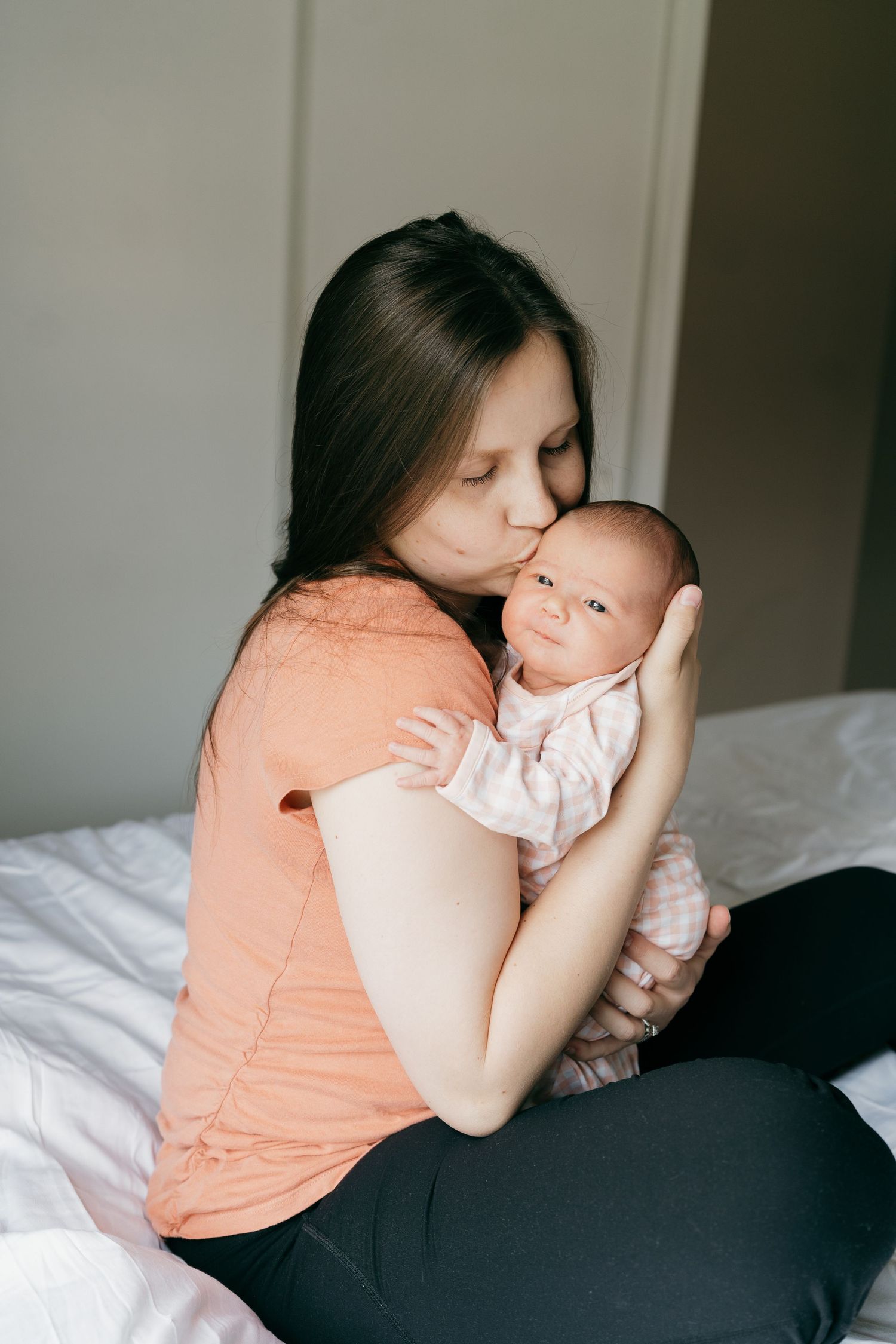 Tender moment of parent cradling sleeping newborn on bed in soft natural light.