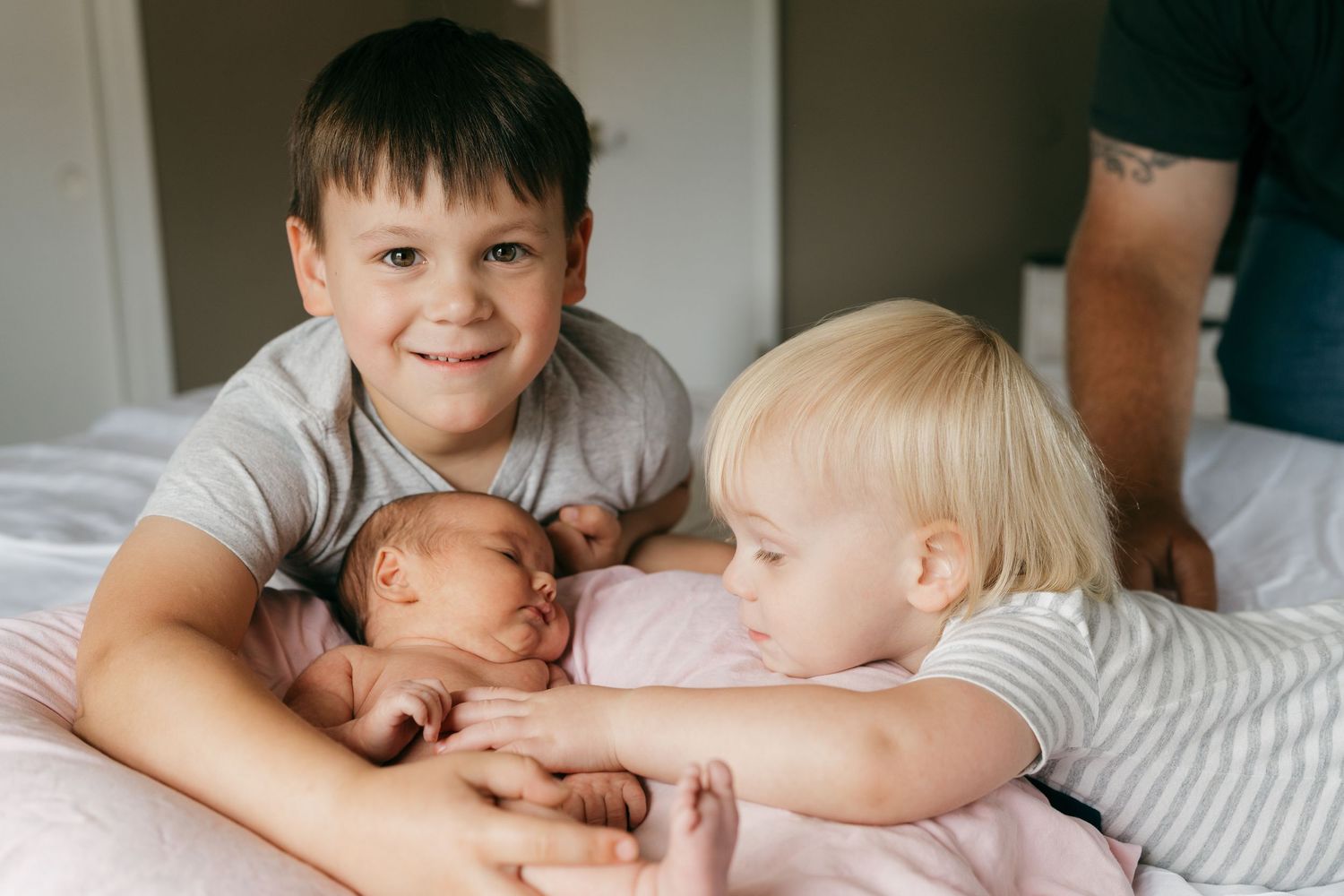 Siblings spending quality time with new baby on comfortable bed.