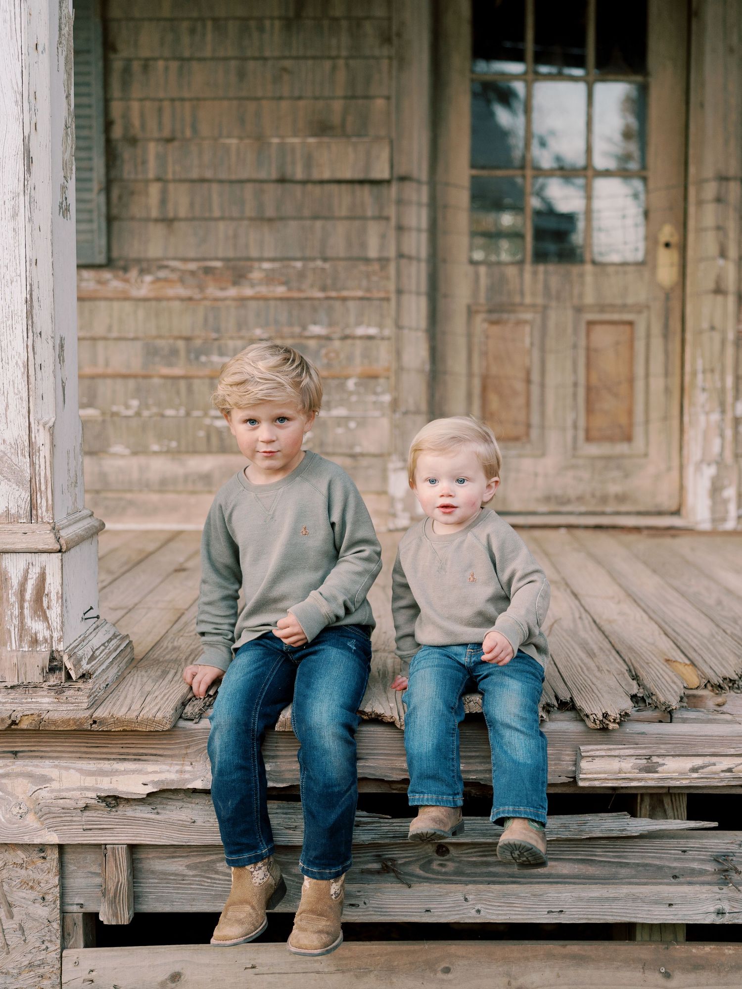 Two children in matching outfits sit on weathered wooden porch steps.