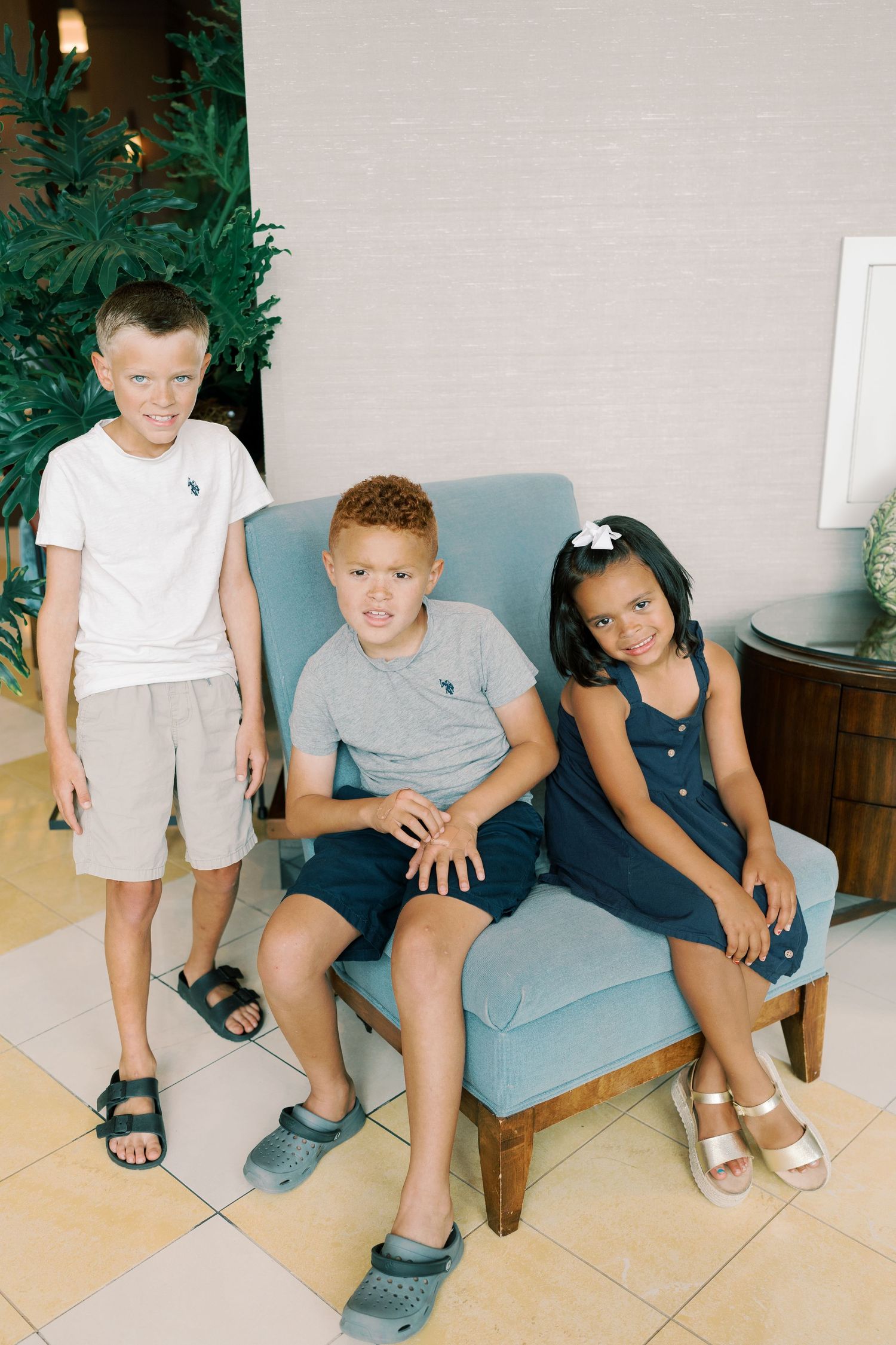 Children sitting together on a light blue bench in casual summer outfits.