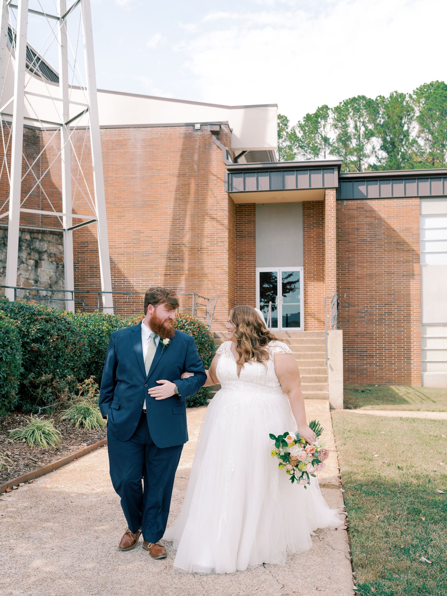 A wedding couple stands together outside a brick building during their autumn ceremony.