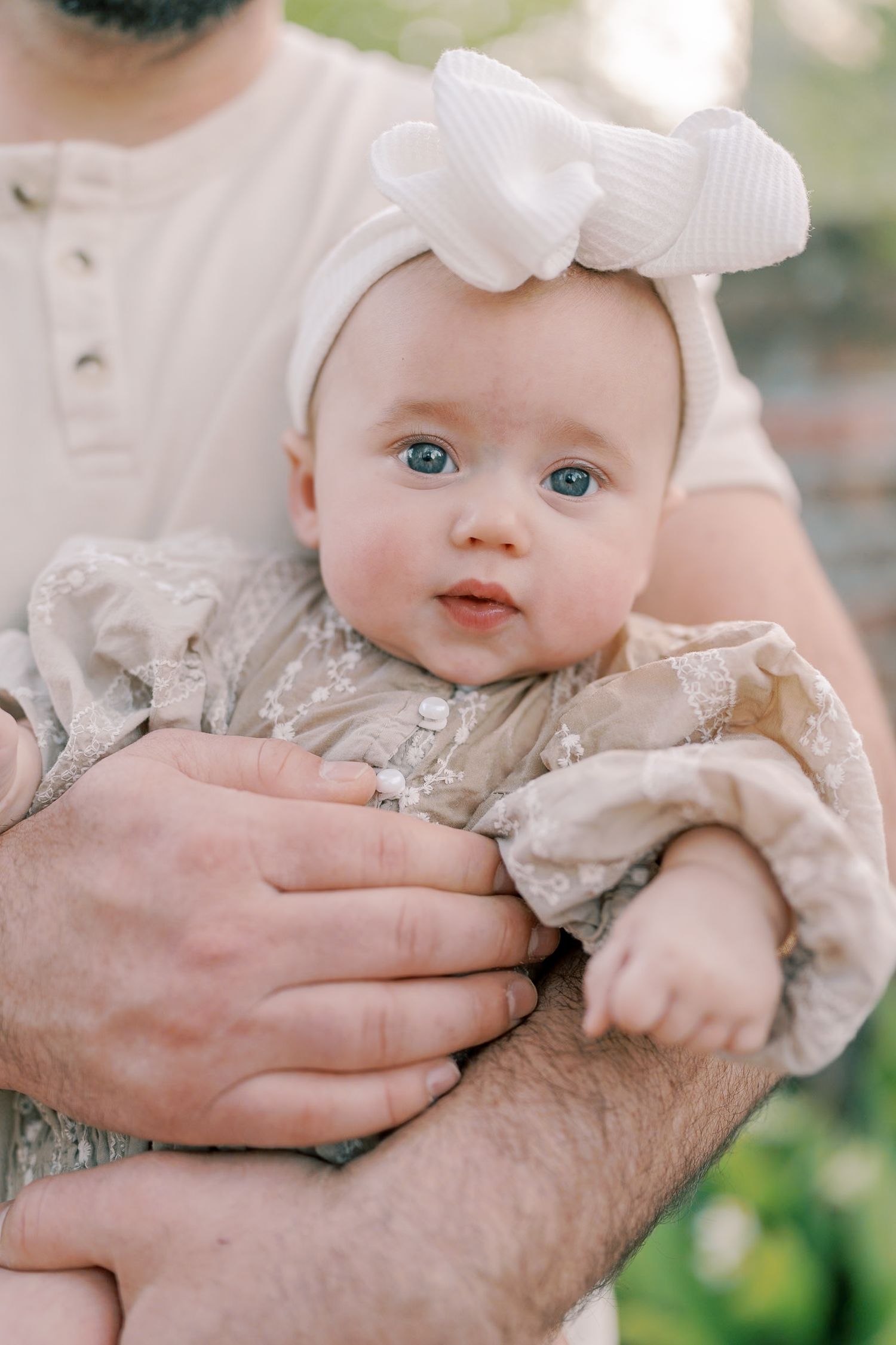 A close-up portrait highlighting bright blue eyes and a white bow against natural lighting.