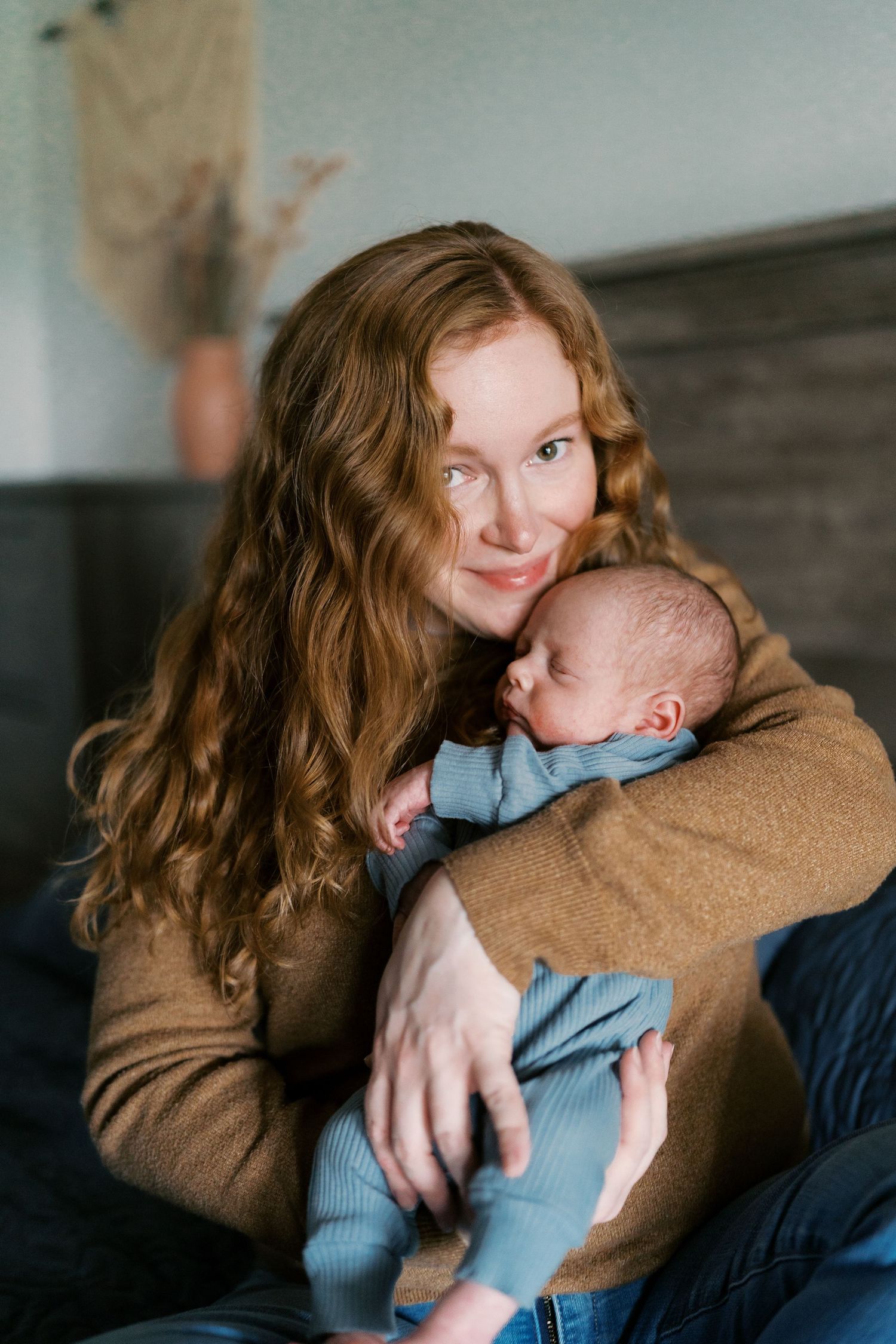 Parent holding baby in cozy brown sweater against dark background.