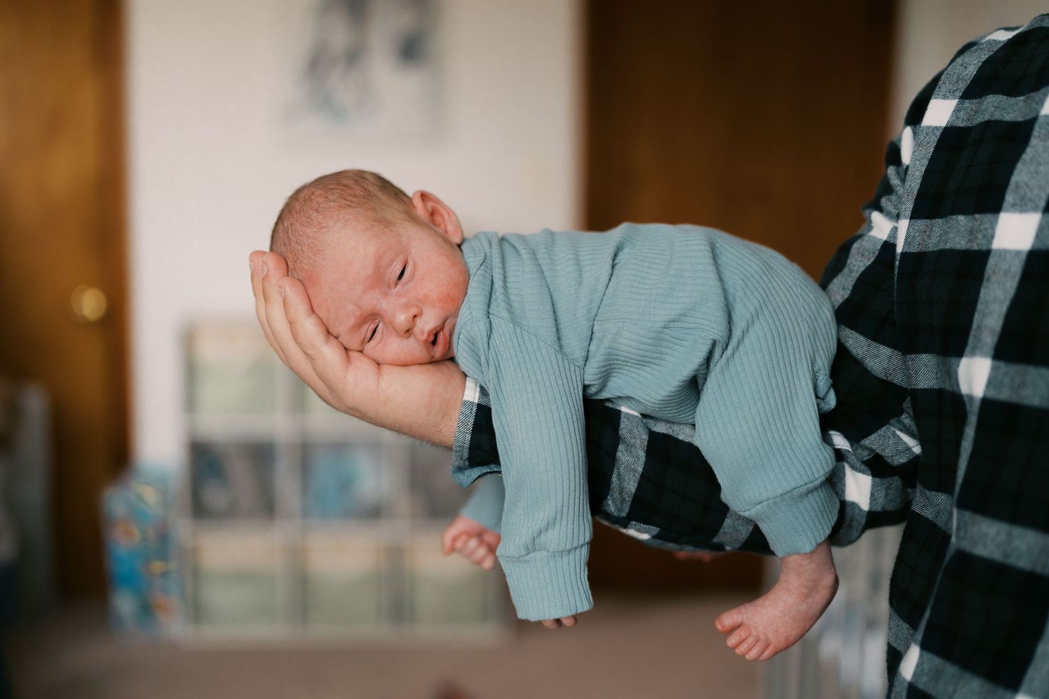 Baby wearing light blue outfit lying on soft surface in natural lighting.
