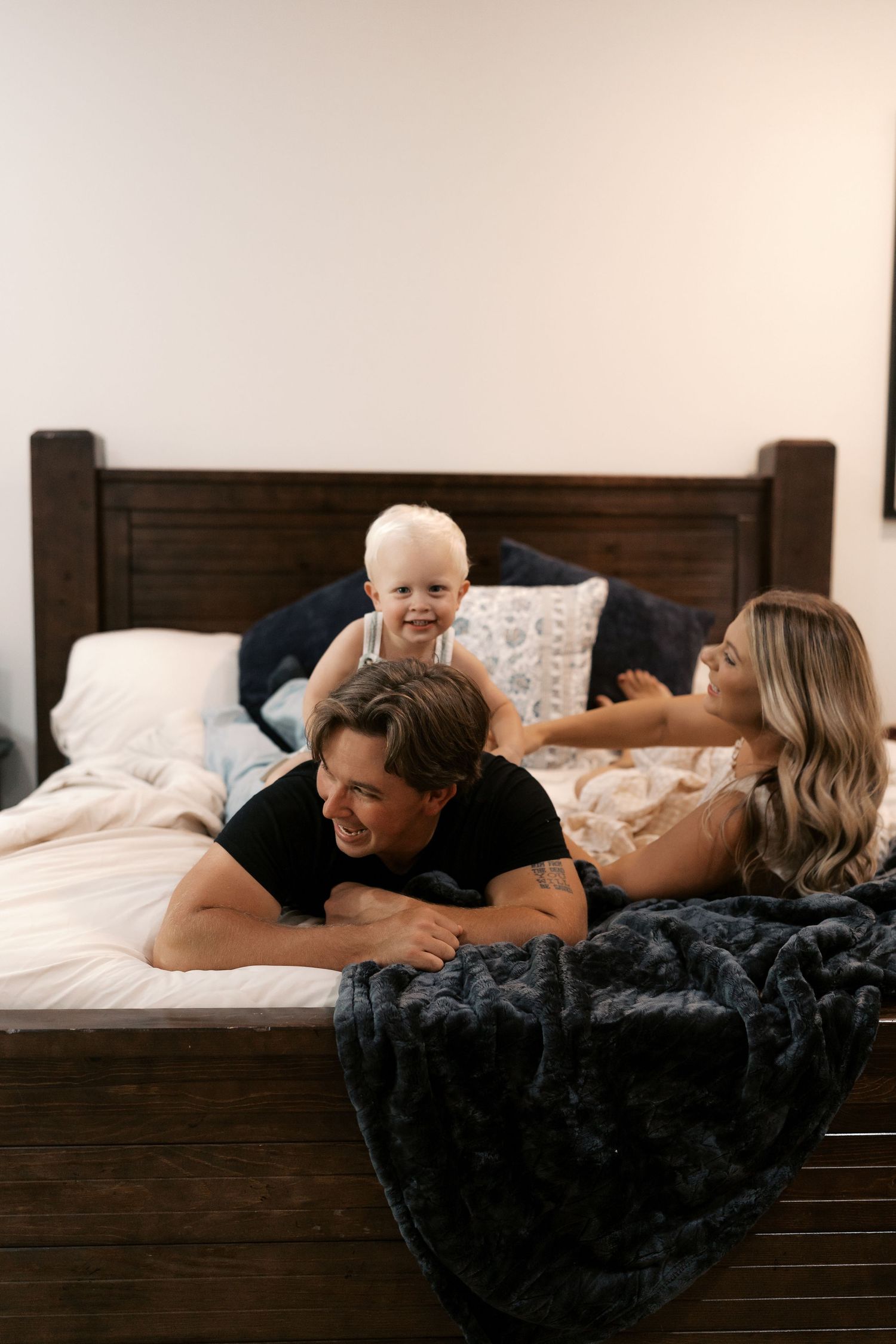 Intimate family moments captured on a wooden bed with dark bedding.