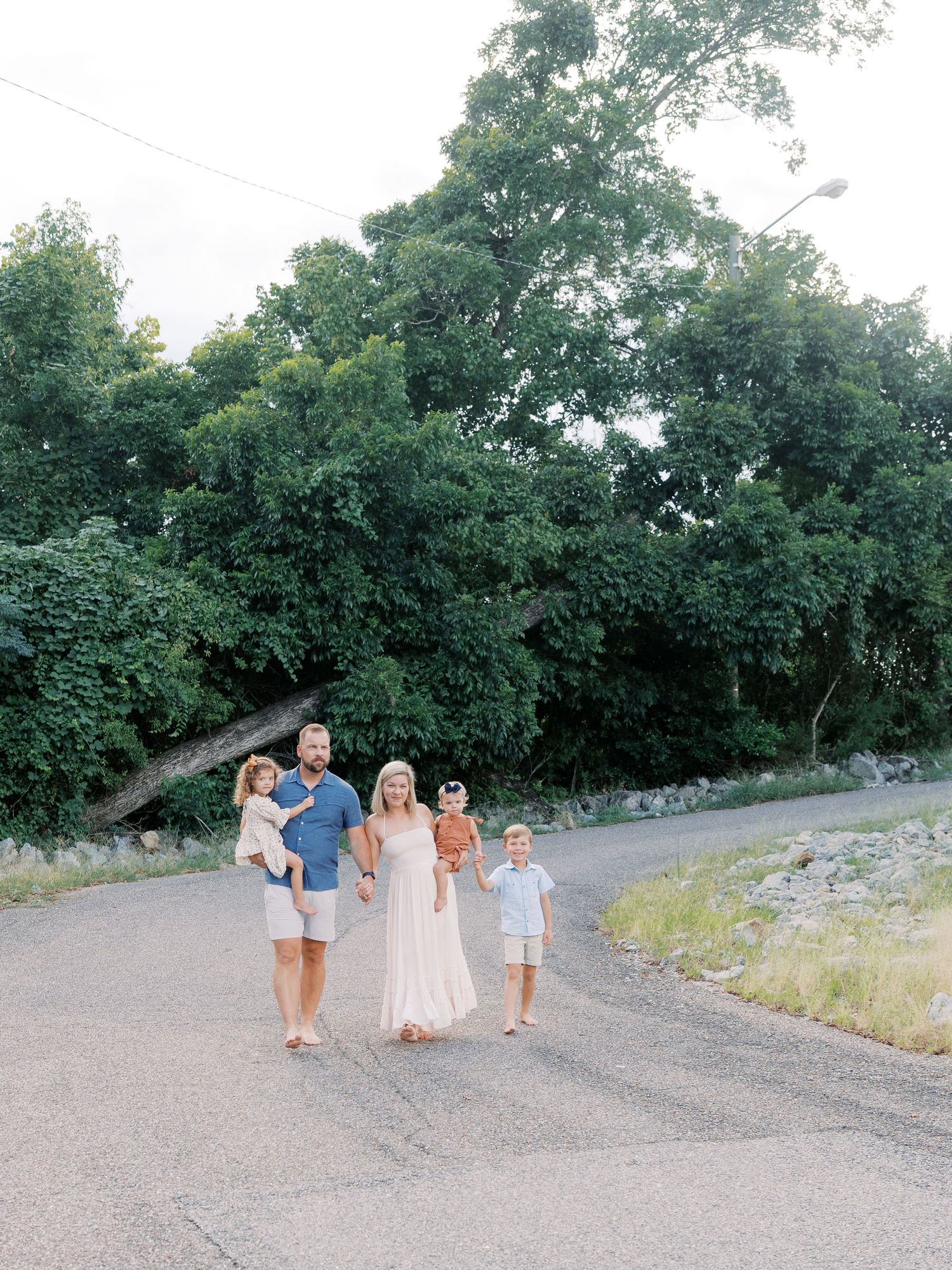A family walks together on a gravel path surrounded by green trees on a summer day.