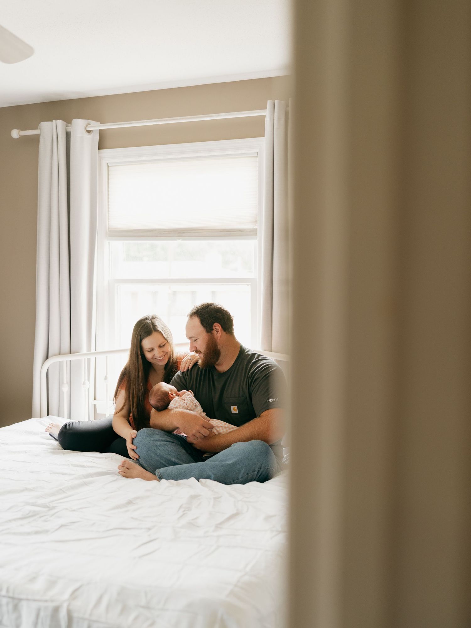 Tender family moment photographed on white bed with natural window lighting.