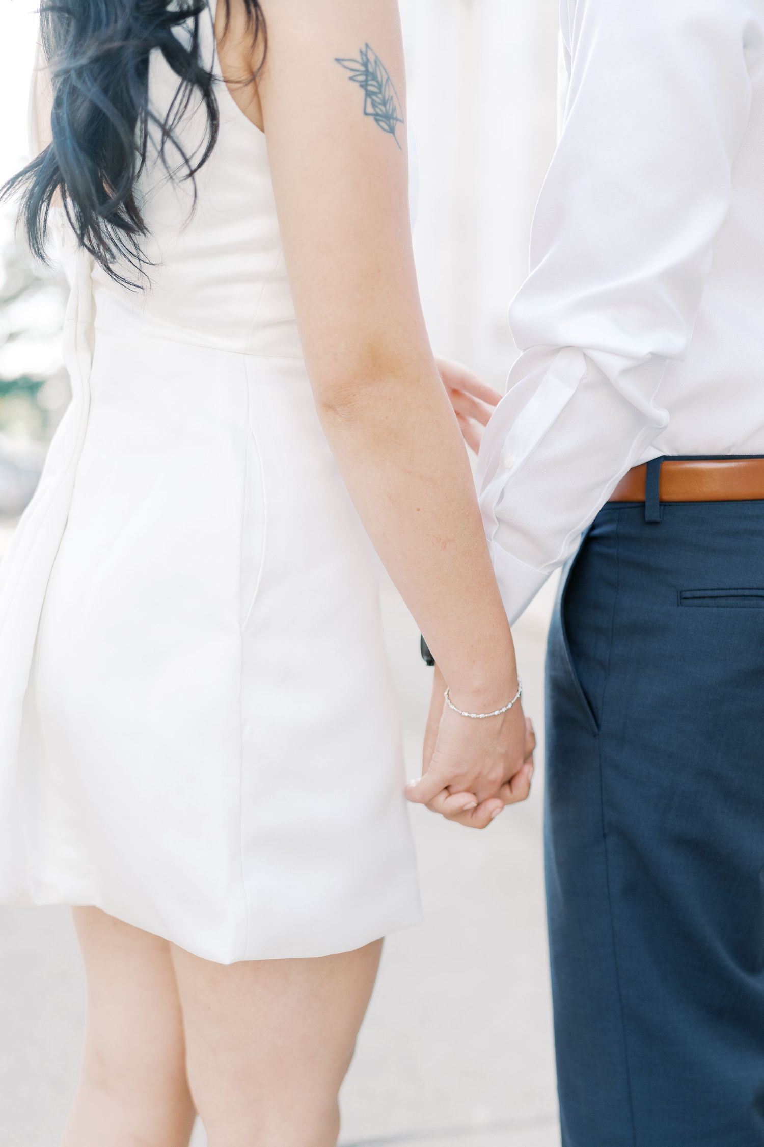 Close-up details of a couple in white and navy outfits holding hands against a bright background.