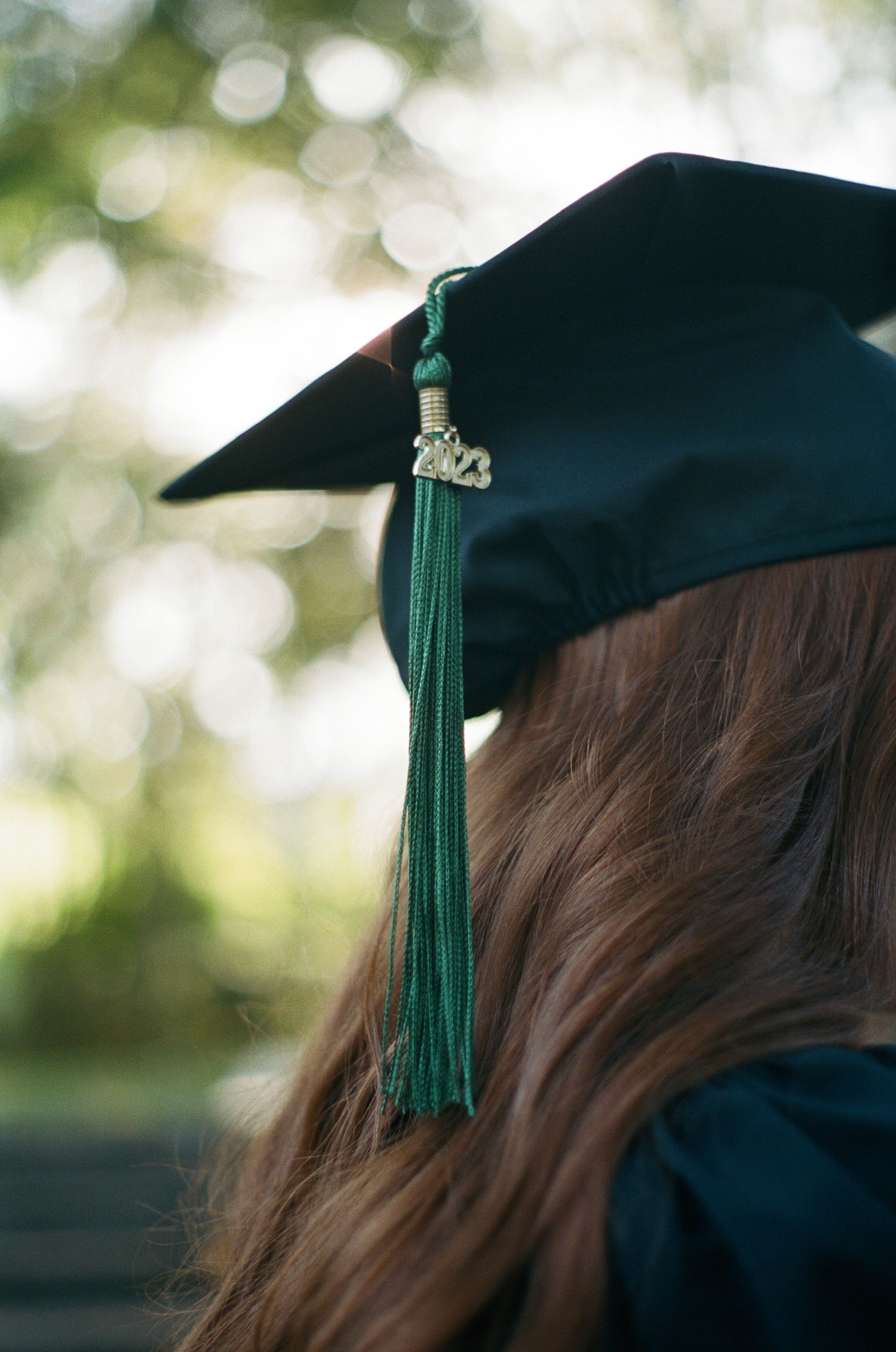Close-up detail of graduation cap with green tassel against blurred background.