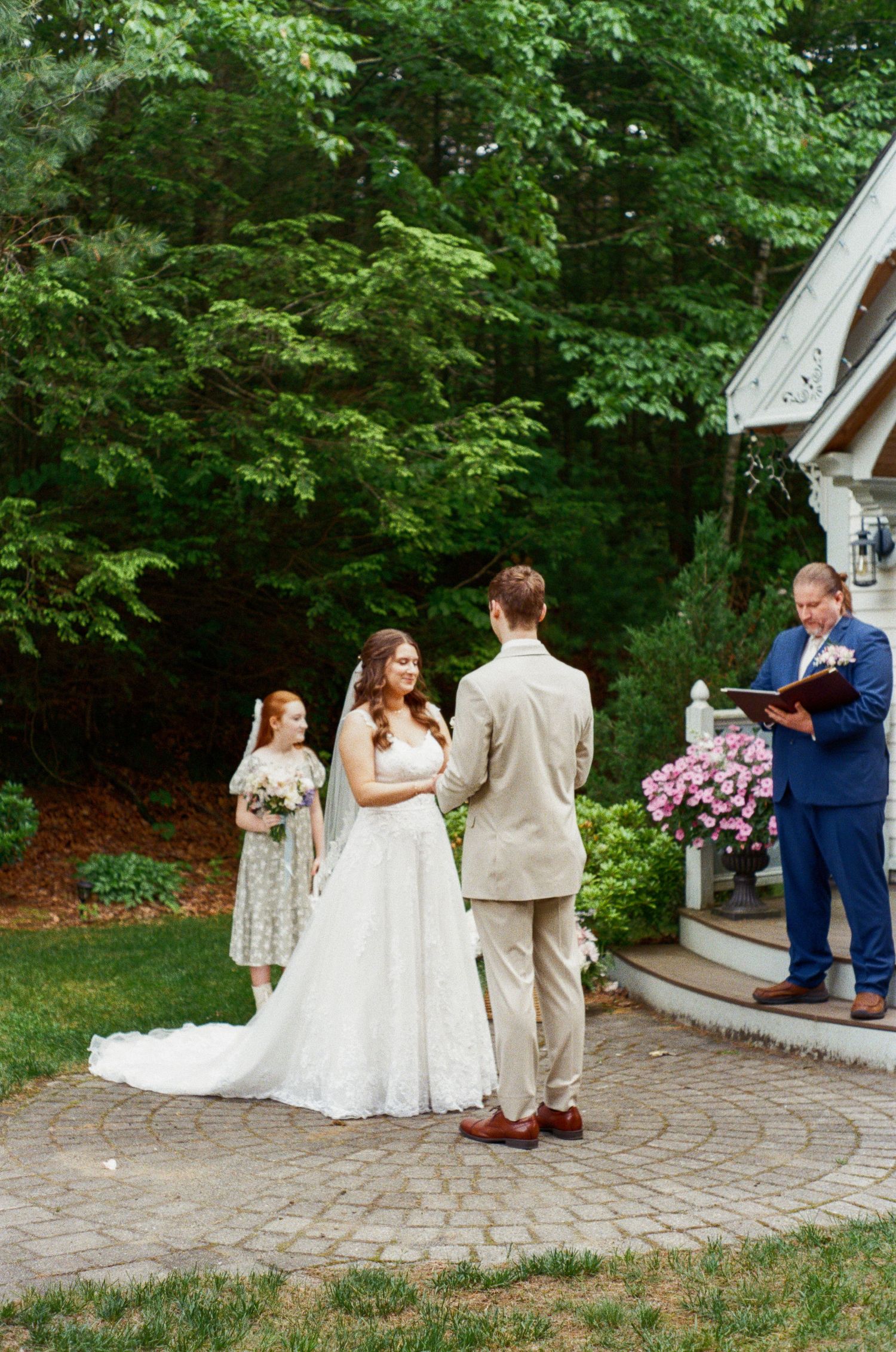 Wedding ceremony taking place on stone patio outside white chapel building.