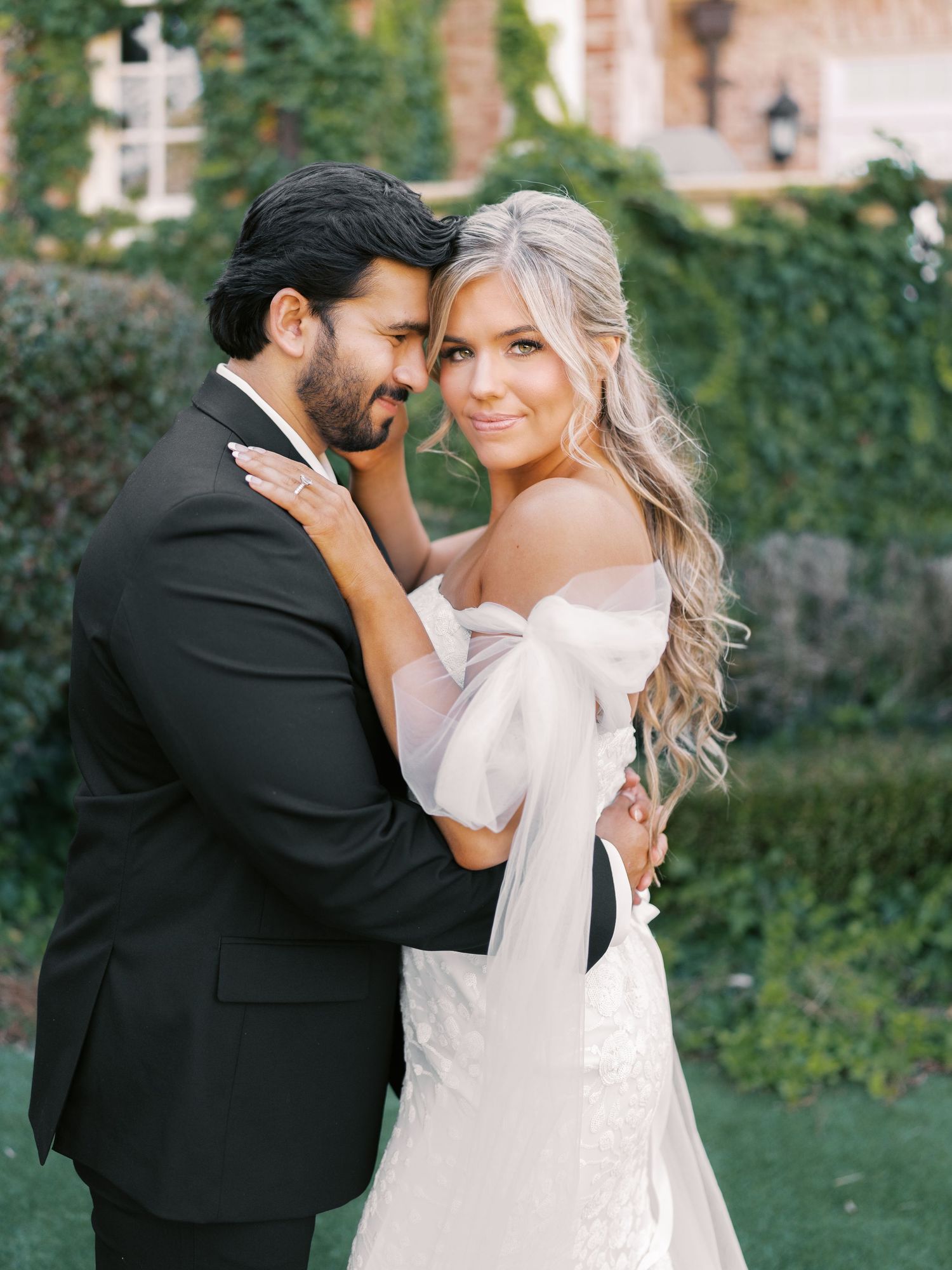 Romantic wedding portrait in garden setting with elegant white dress and black tuxedo.