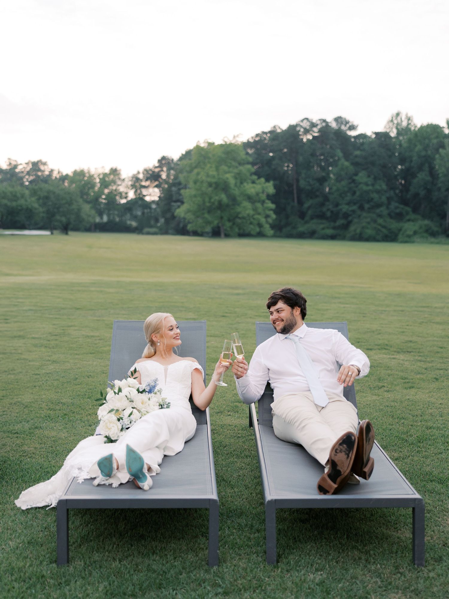 Wedding couple lounging on gray benches in outdoor setting with bouquet.