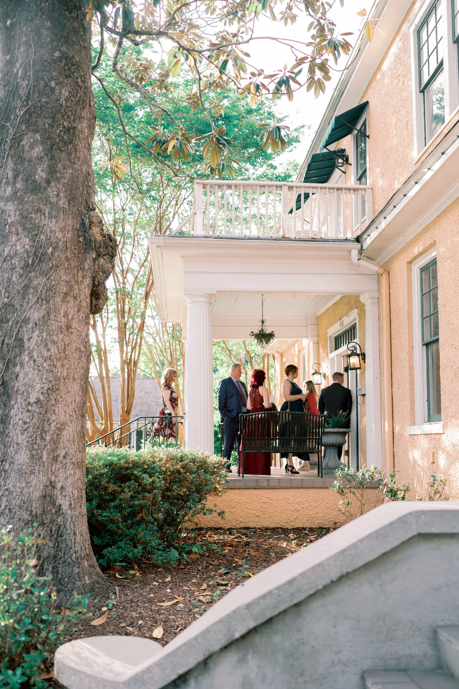 Covered porch walkway of a historic building with large trees and landscaping in the foreground.