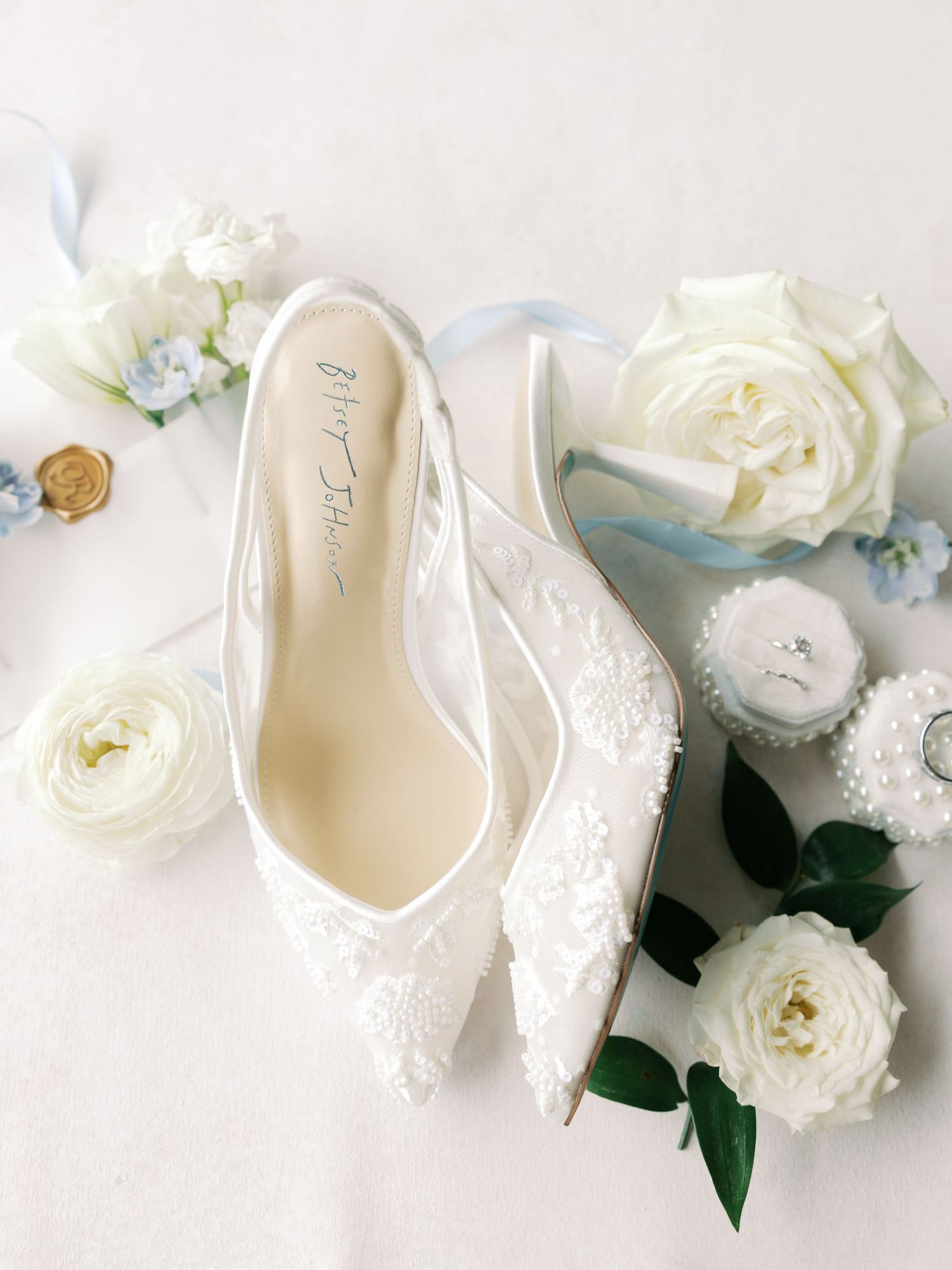 White bridal shoes surrounded by delicate white roses and blue floral accents.