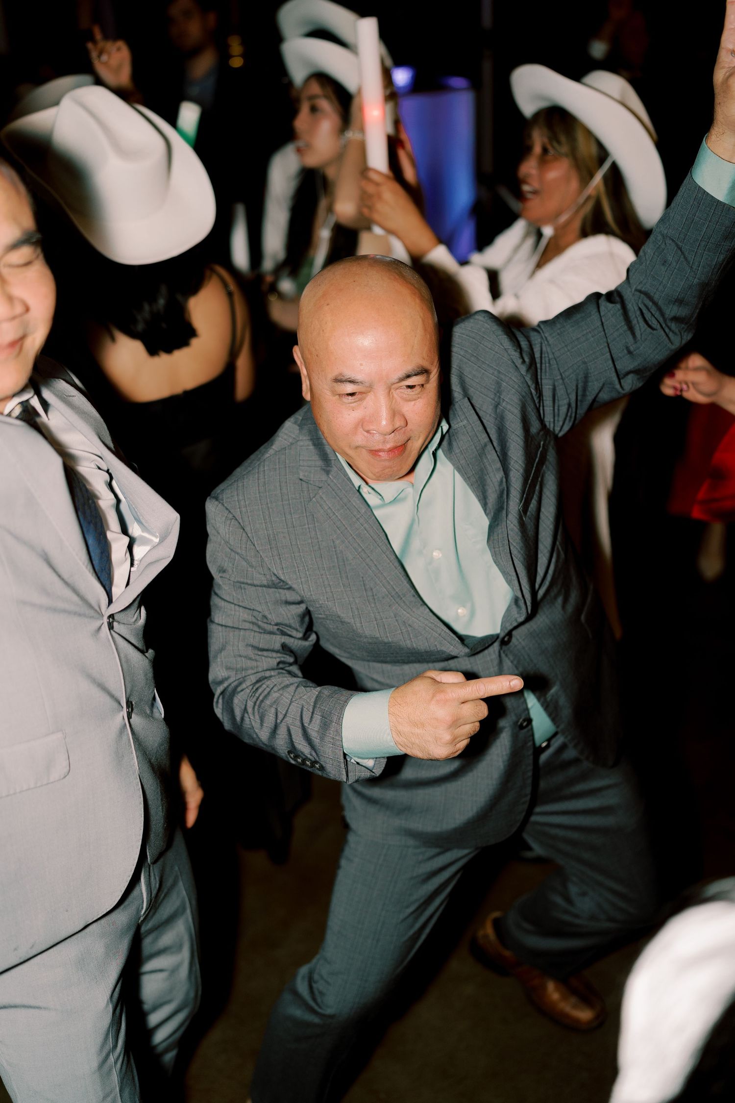 Person in grey suit and white cowboy hat dancing enthusiastically at a party.
