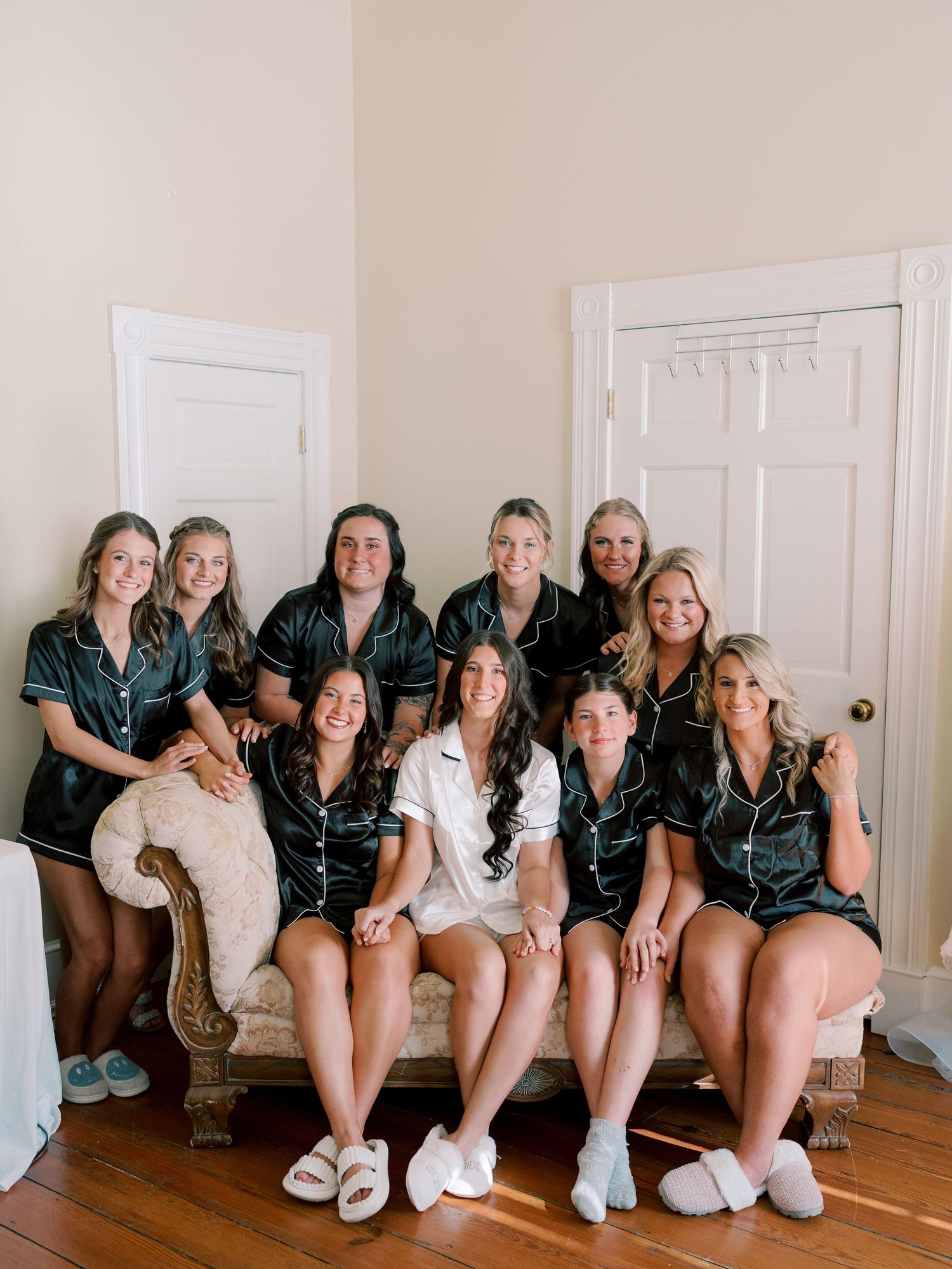 Bridal party wearing matching silk robes posing together on antique sofa.
