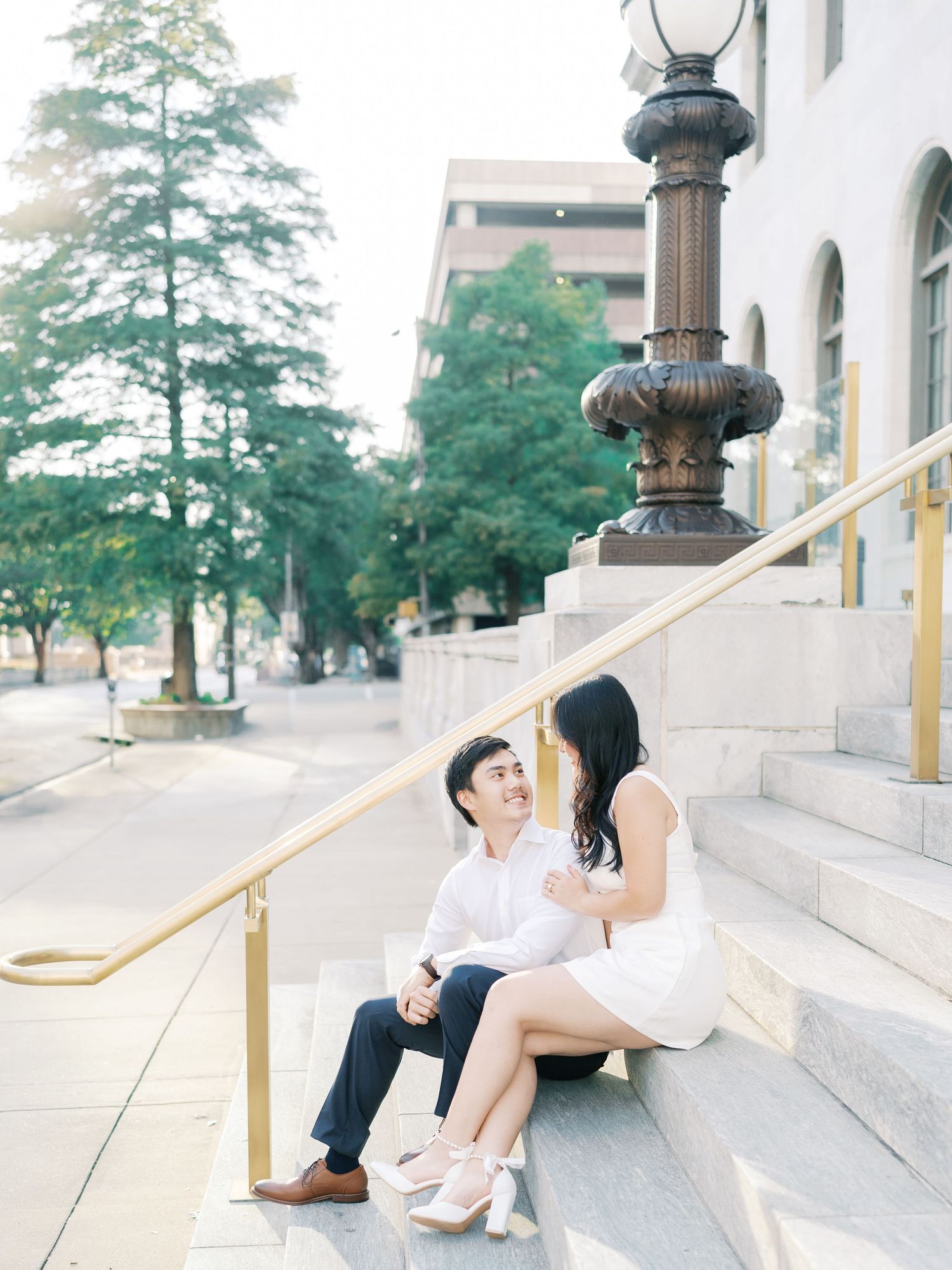Romantic couple posing on white marble steps of a classic building in soft natural light.