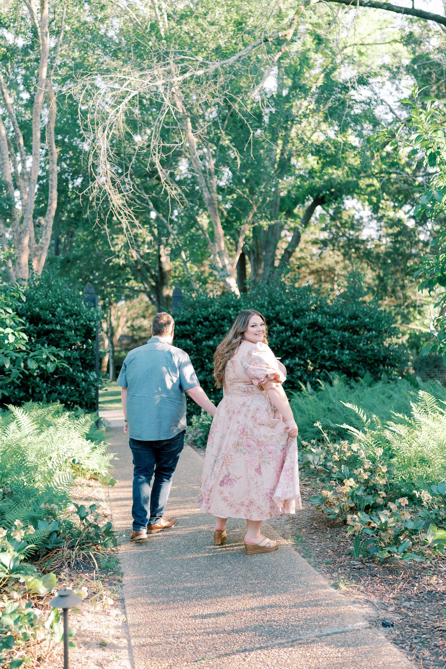 A couple walking hand in hand down a tree-lined garden path.