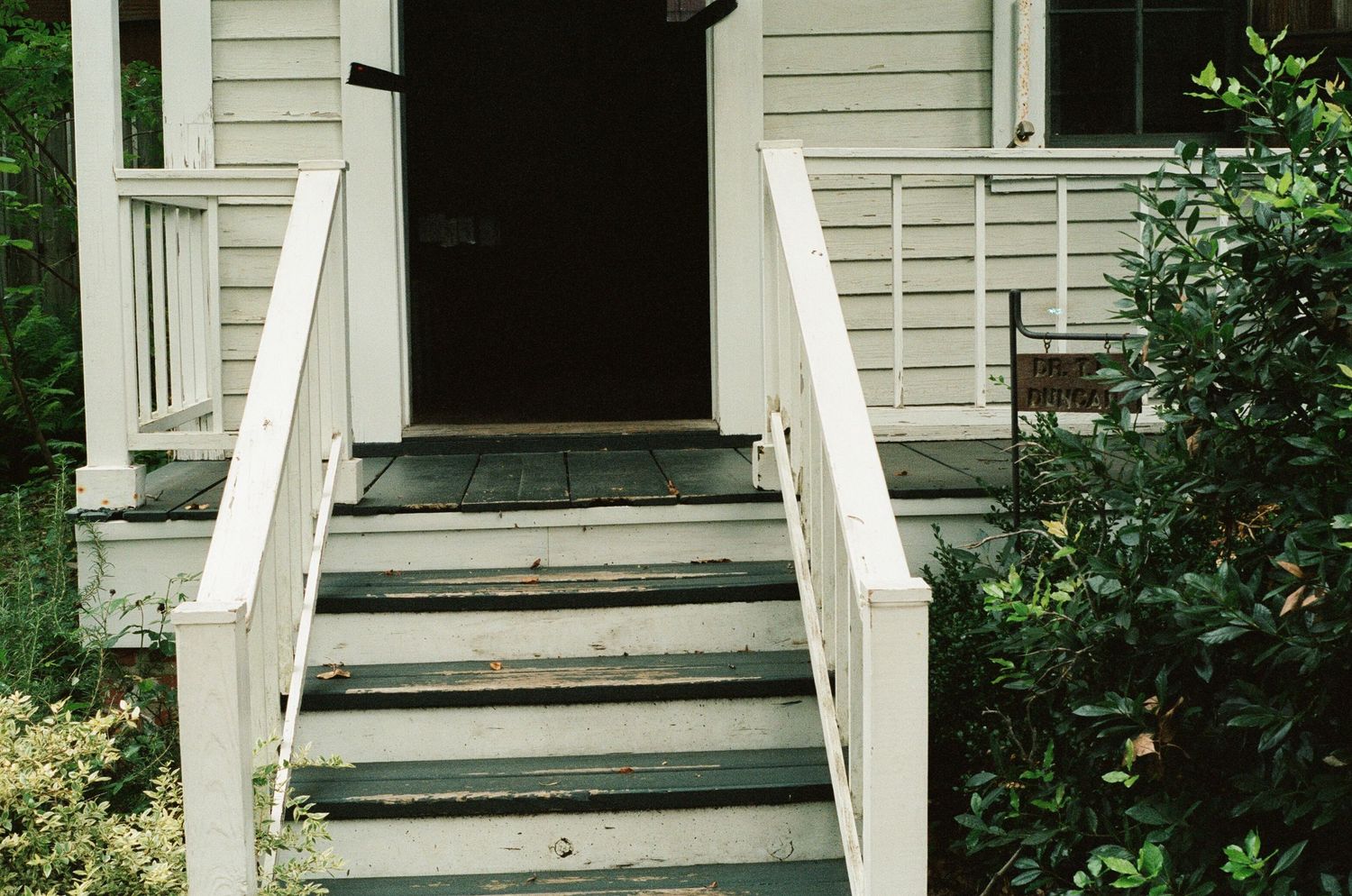 White wooden porch steps leading to a house entrance with green landscaping.