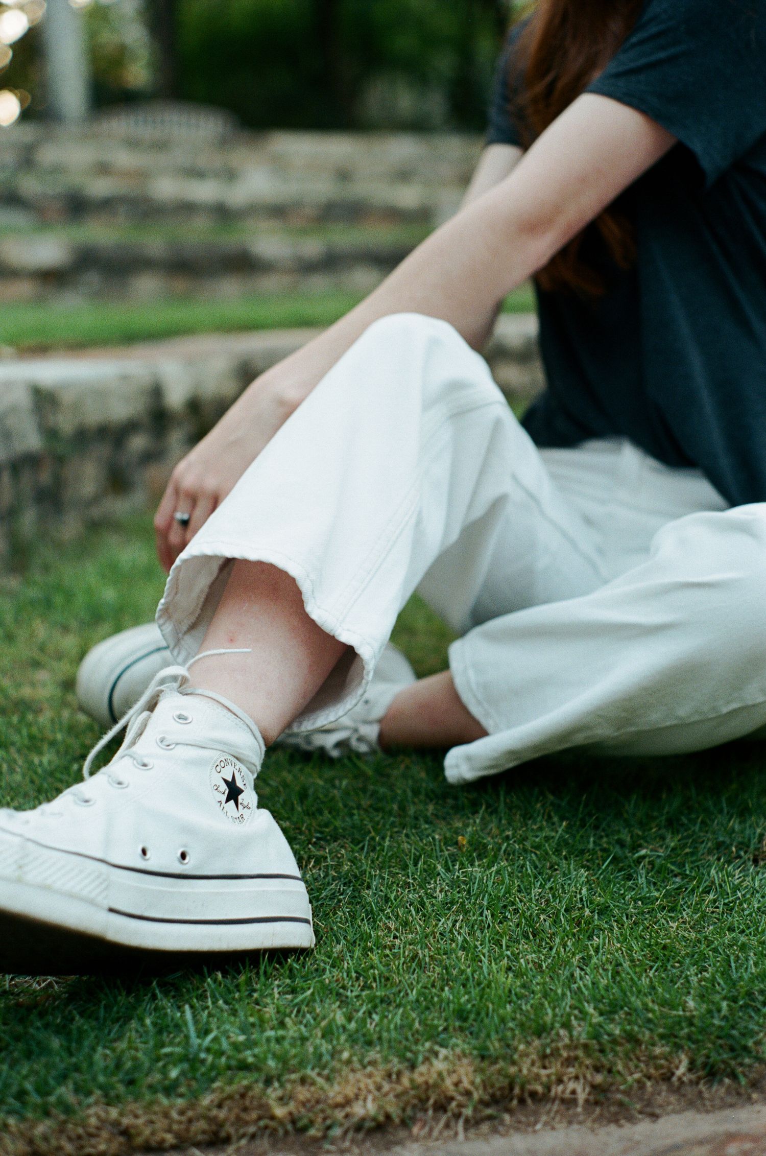 White Converse sneakers and casual outfit detail shot on green grass.