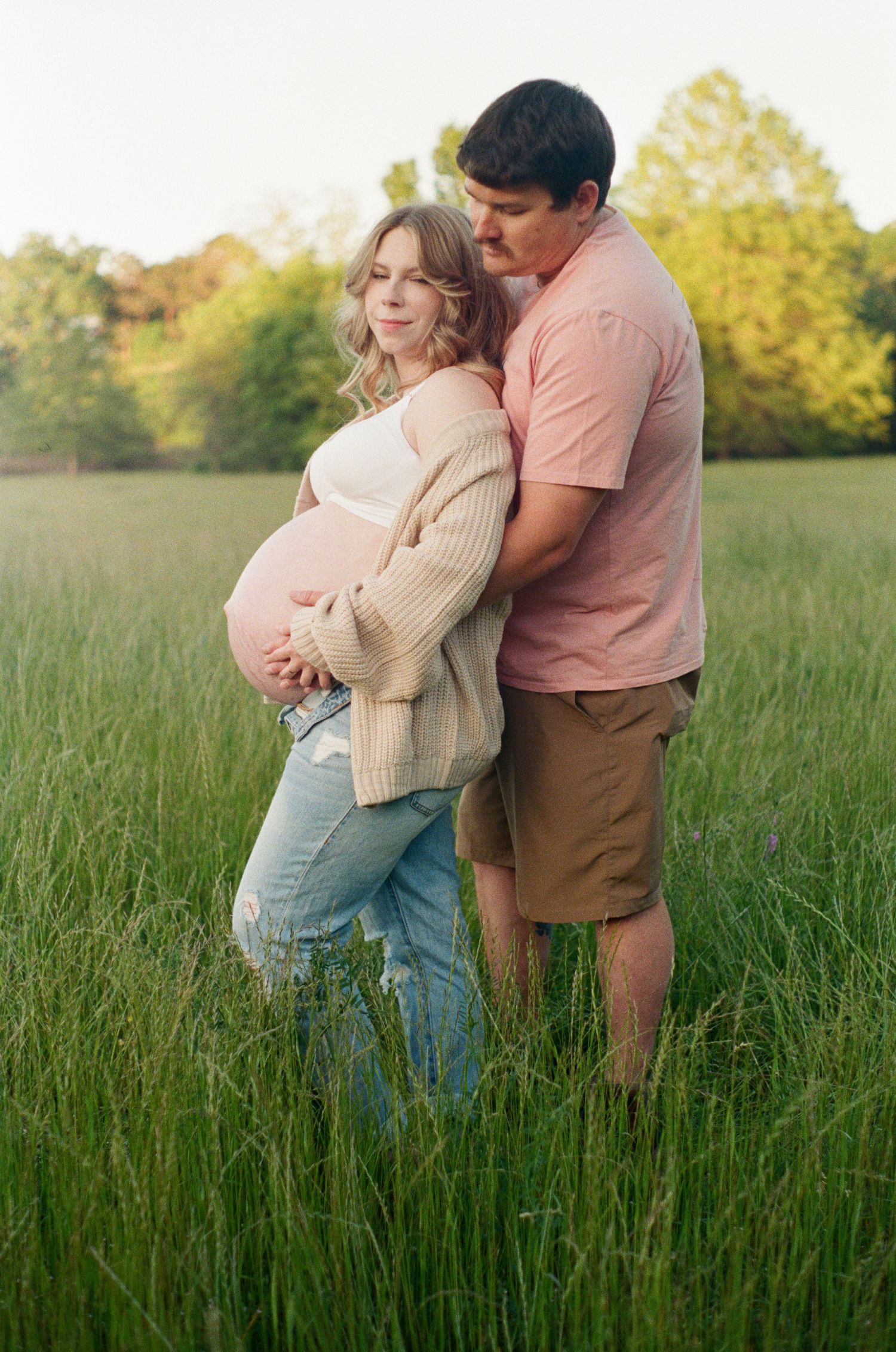 Couple sharing intimate moment in sunlit meadow with tall grass.