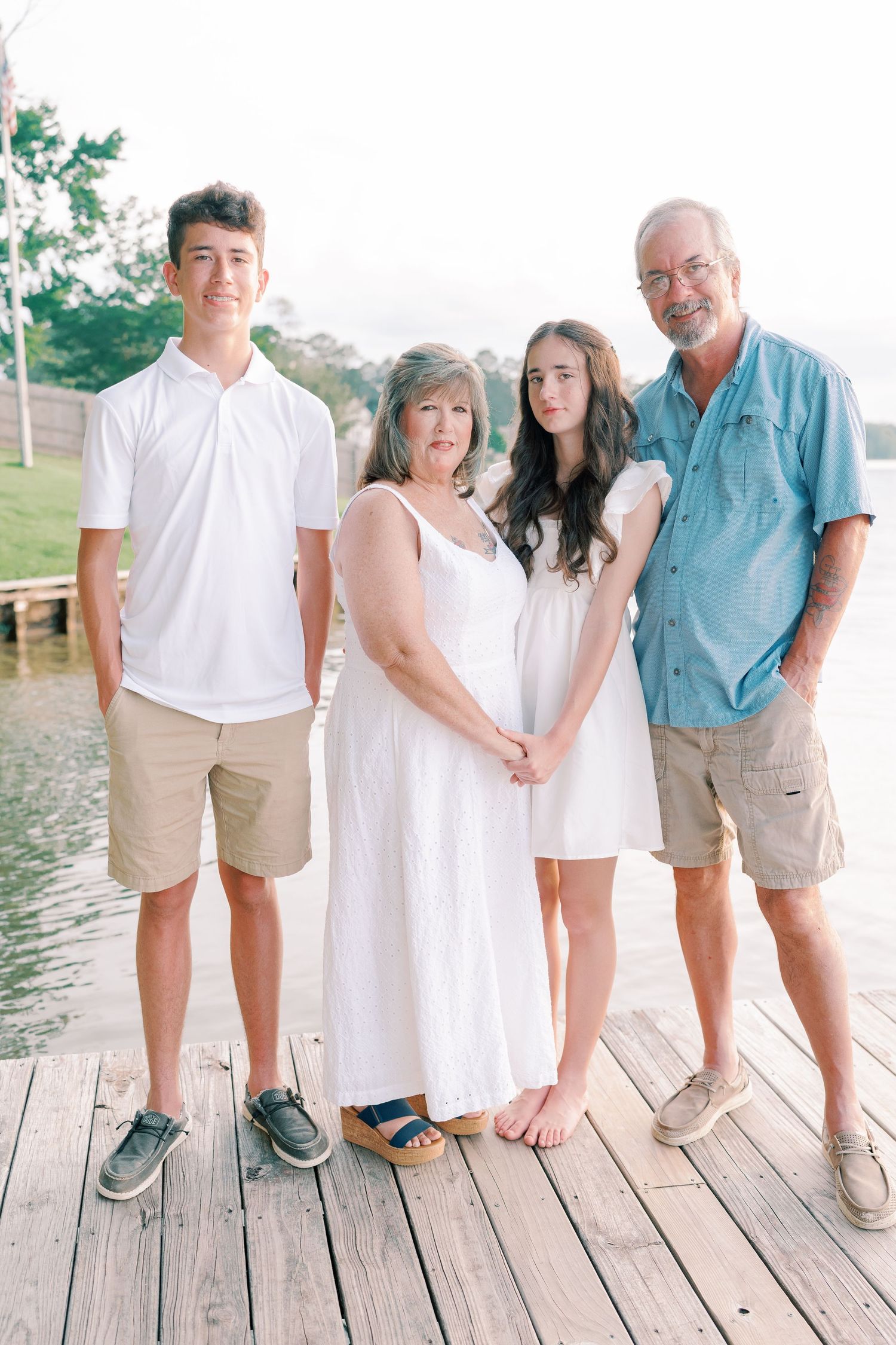 Family wearing coordinated white and khaki outfits poses on wooden dock by the water.