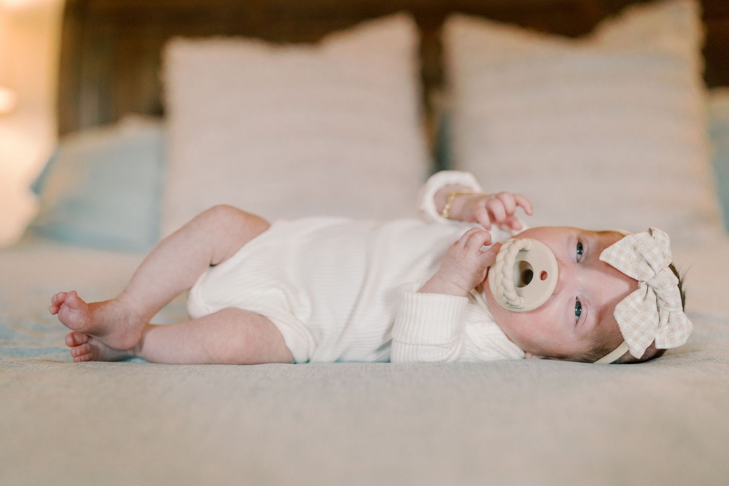 Side view of baby resting on white bedding in natural light.