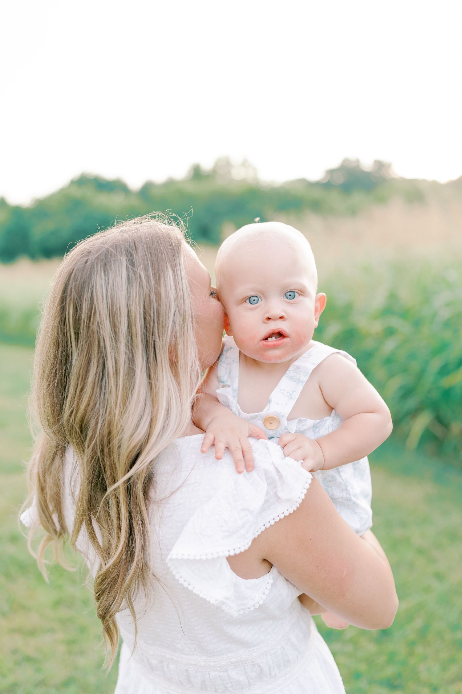 Sweet interaction between parent and infant wearing matching white outfits in a sunlit field.
