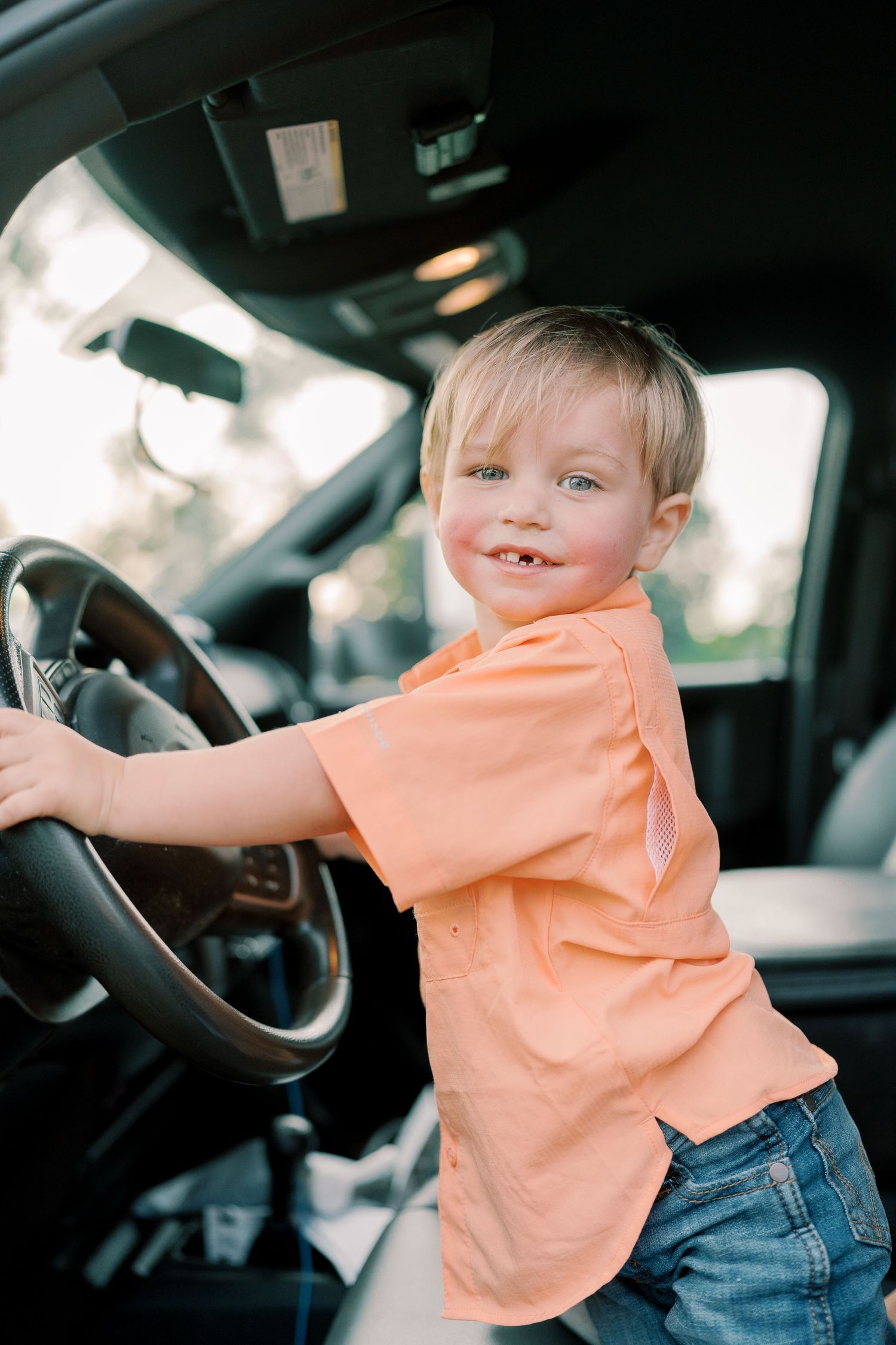 Young person pretending to drive while sitting in car driver's seat.