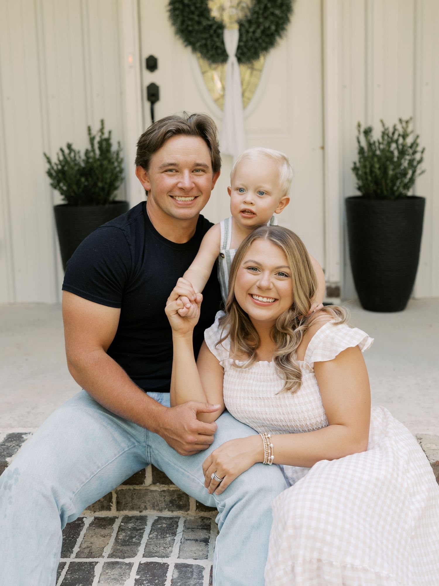 A couple shares a joyful moment while sitting on outdoor steps with wreaths and planters.