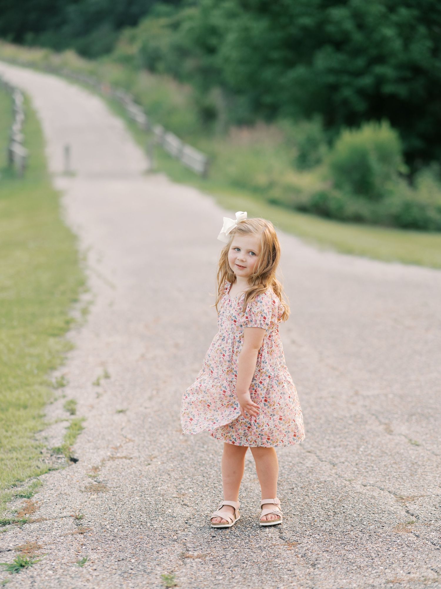 Small child in a floral dress playing and walking on a gravel path outdoors.