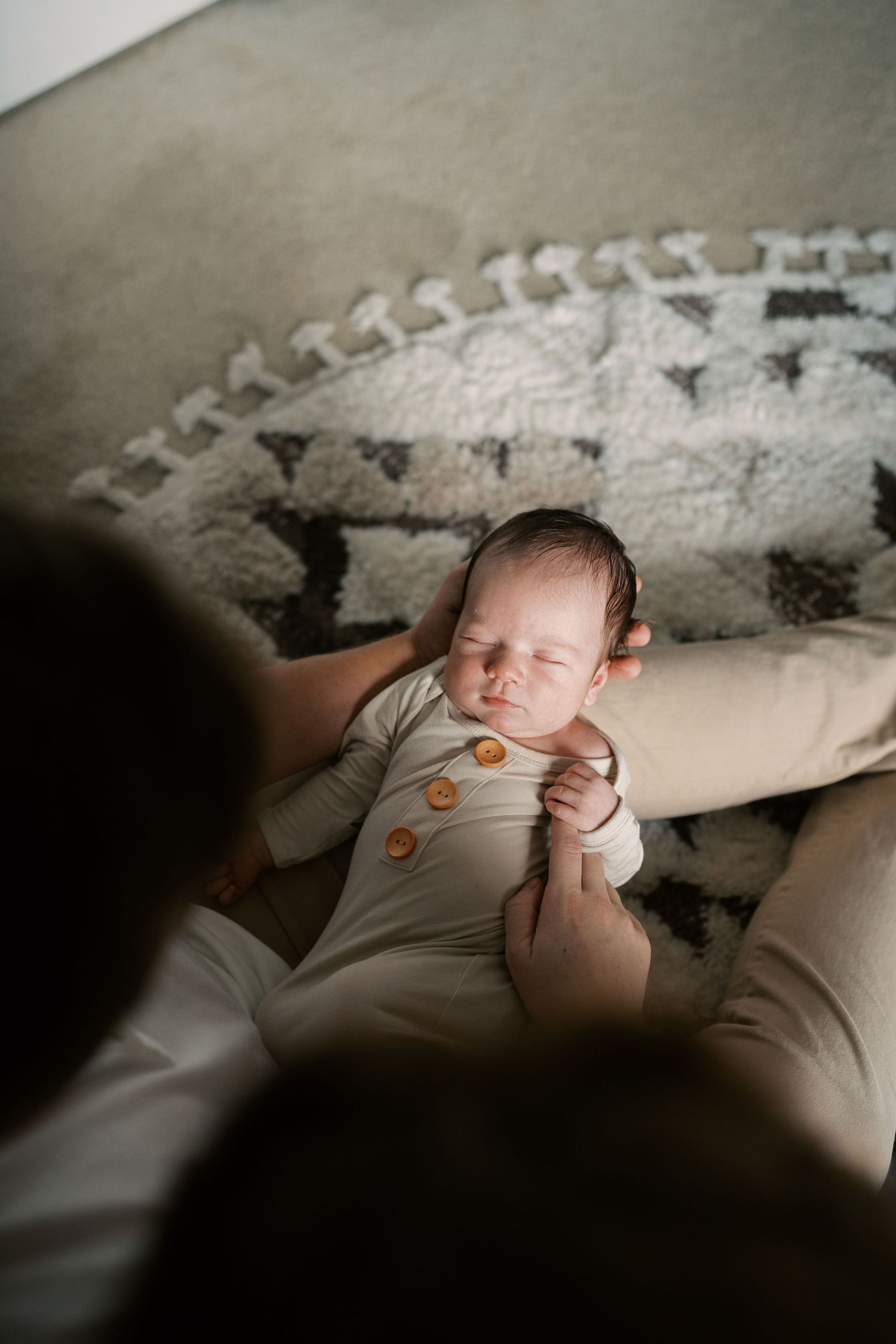 Peaceful newborn baby wearing neutral colored onesie resting in gentle shadows.