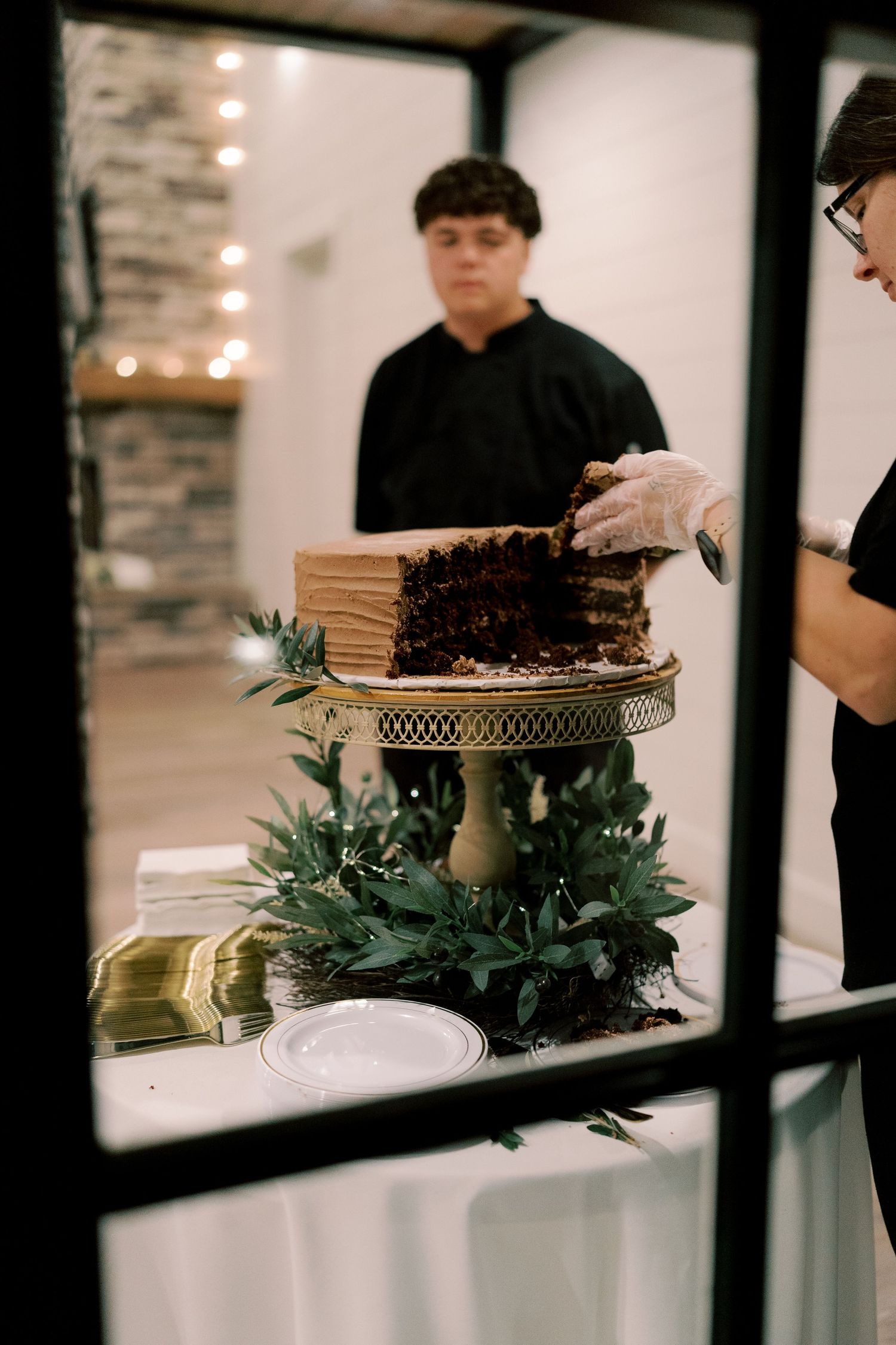 Dessert table with chocolate cake and greenery decorations at wedding reception.