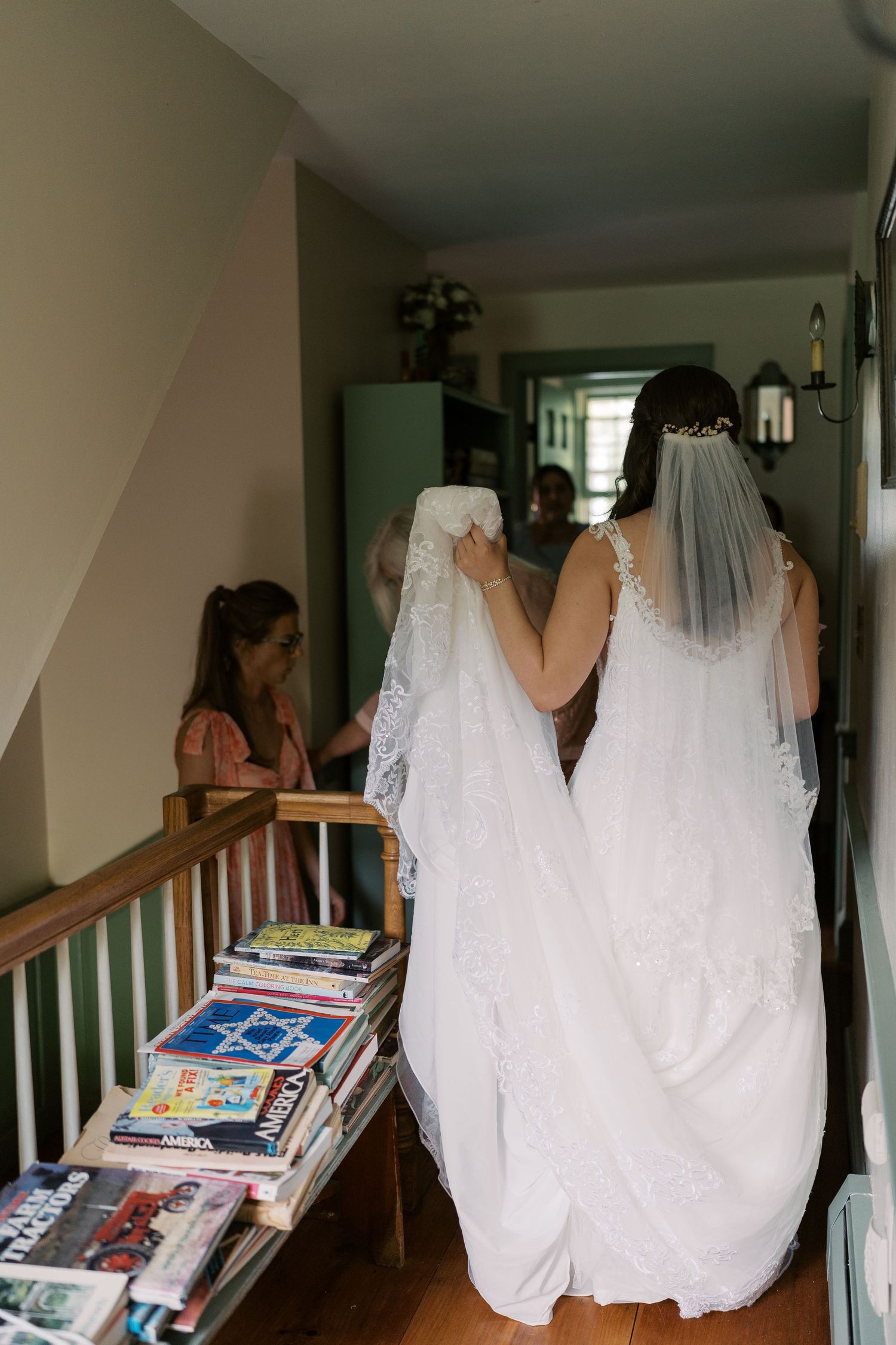 White wedding dress hanging in hallway with books stacked along staircase.