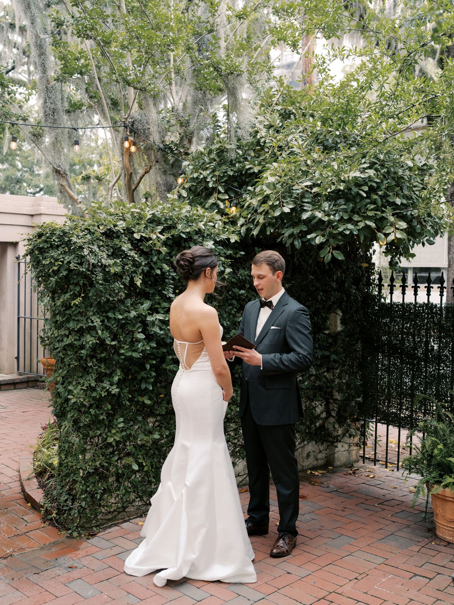Outdoor wedding moment on a brick patio surrounded by green hedges.