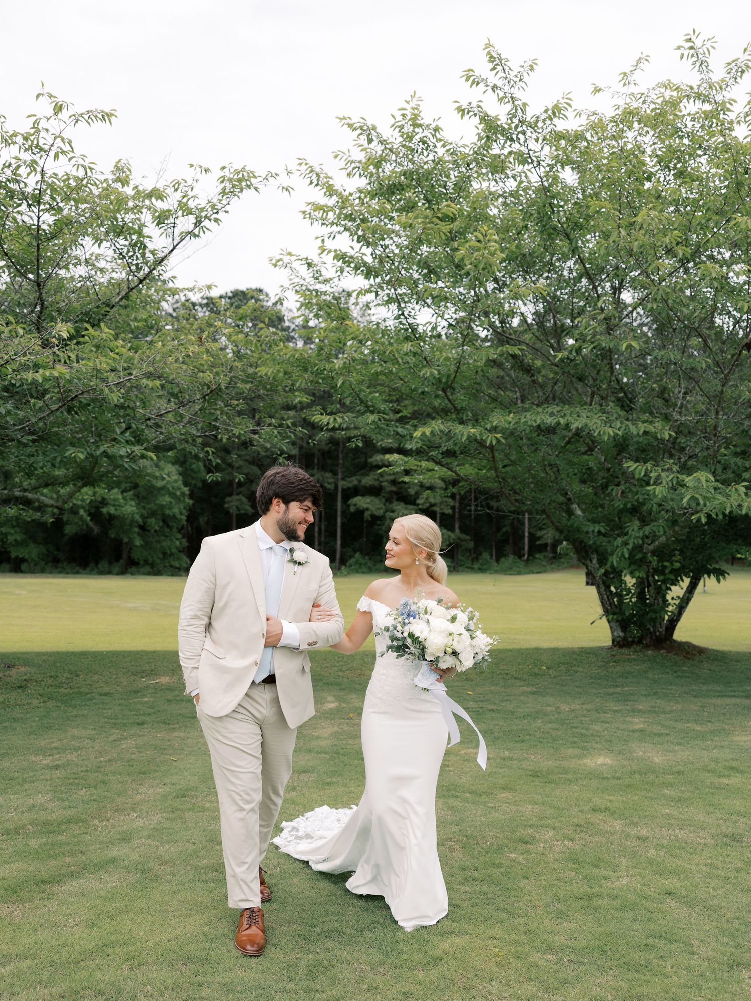 Couple walking and dancing together on grassy lawn during wedding photoshoot.