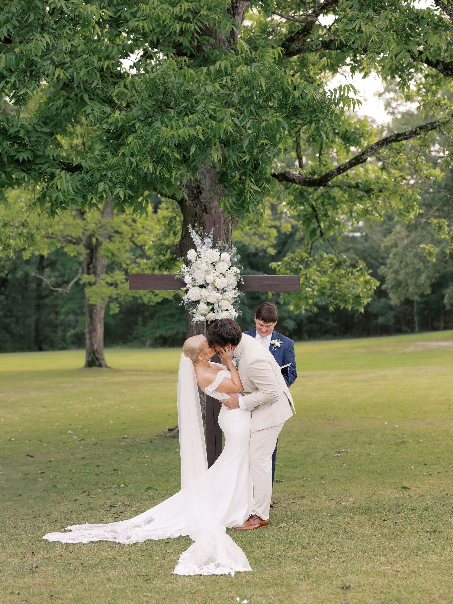 A romantic wedding moment captured on a scenic lawn with lush trees in the background.