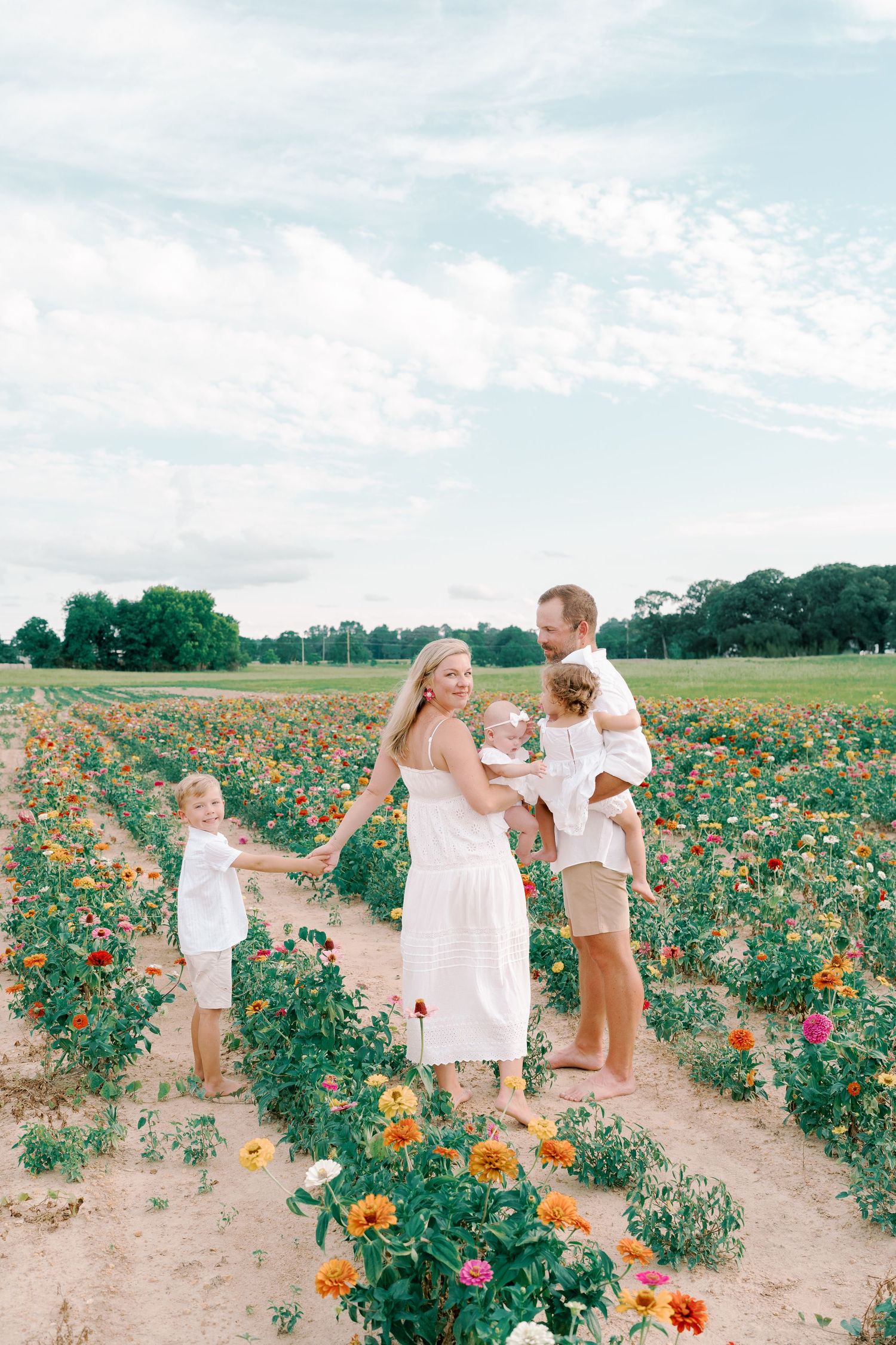 People in light colored clothing dance and play in a vibrant flower field on a bright summer day.